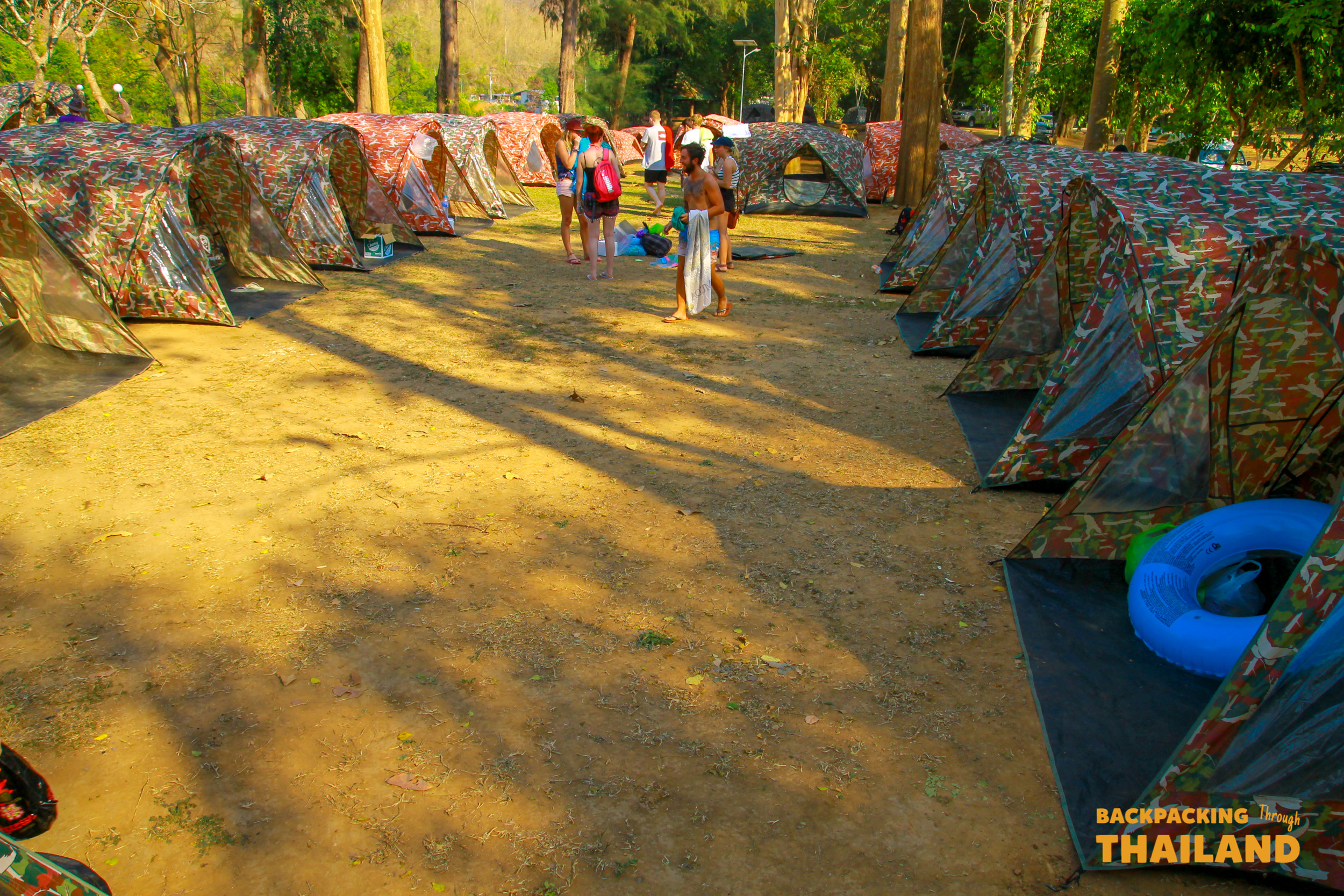Backpacking group walking through a rustic campsite pathway lined with wooden huts