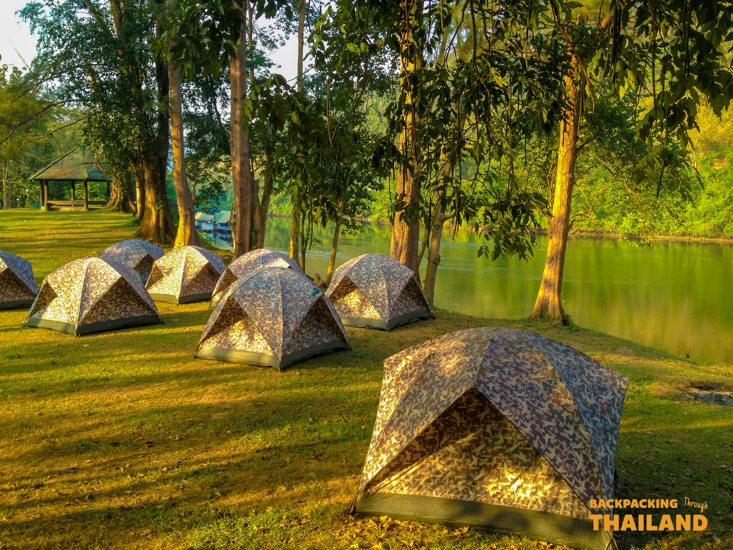 Unique triangular stone bungalows surrounded by trees and reflecting water at the campsite