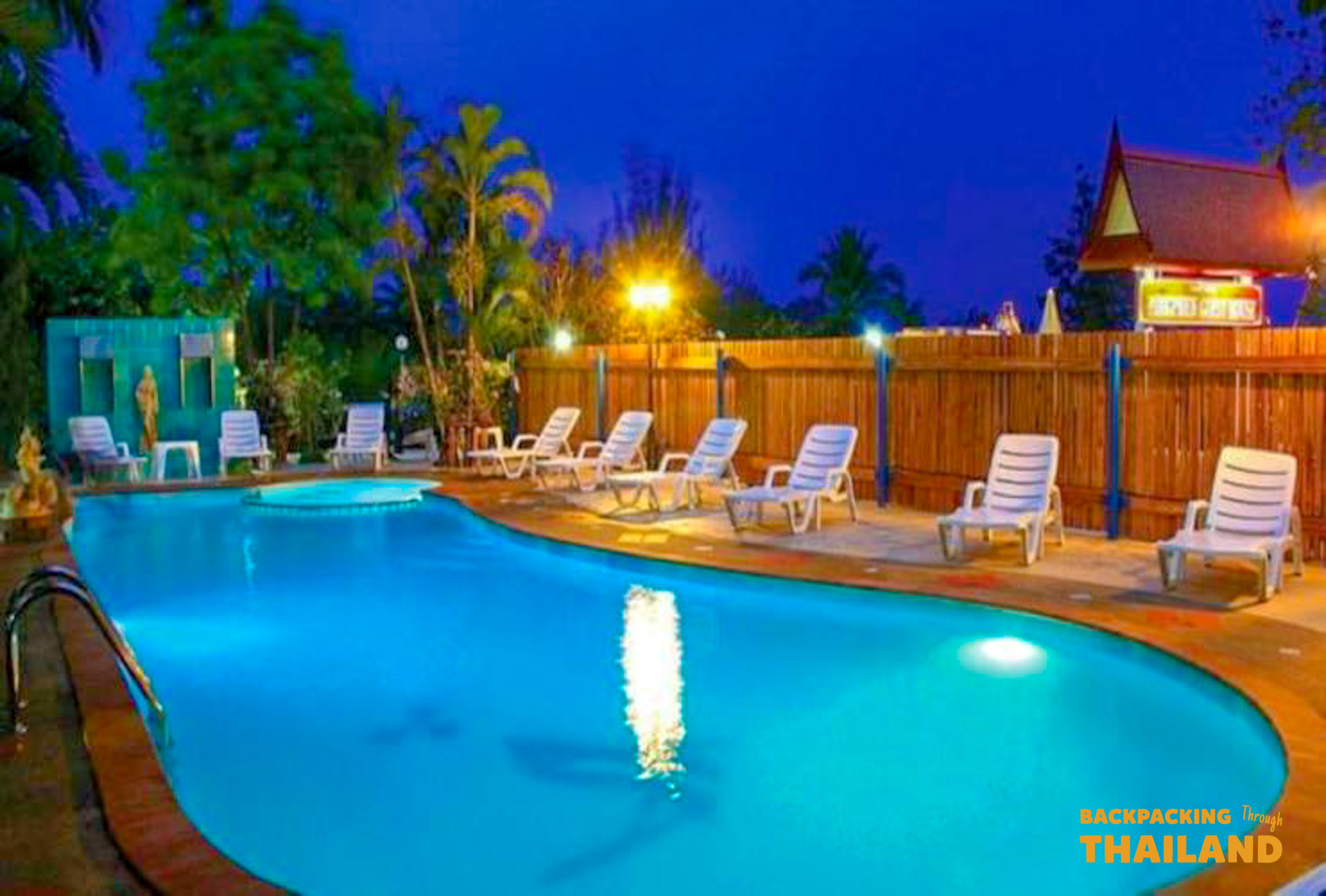 Resort swimming pool with sun loungers and white chairs at night