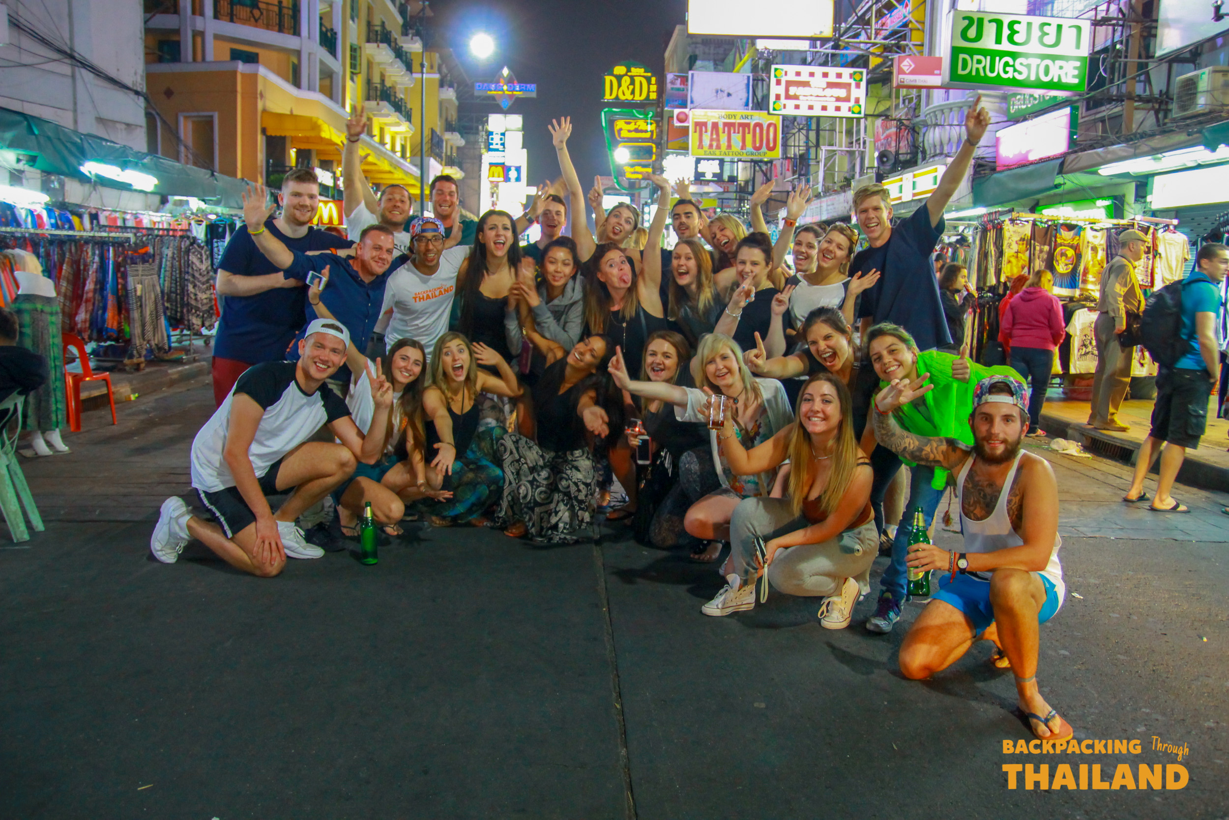 A joyful group of friends celebrating on the vibrant Khao San Road in Bangkok at night.