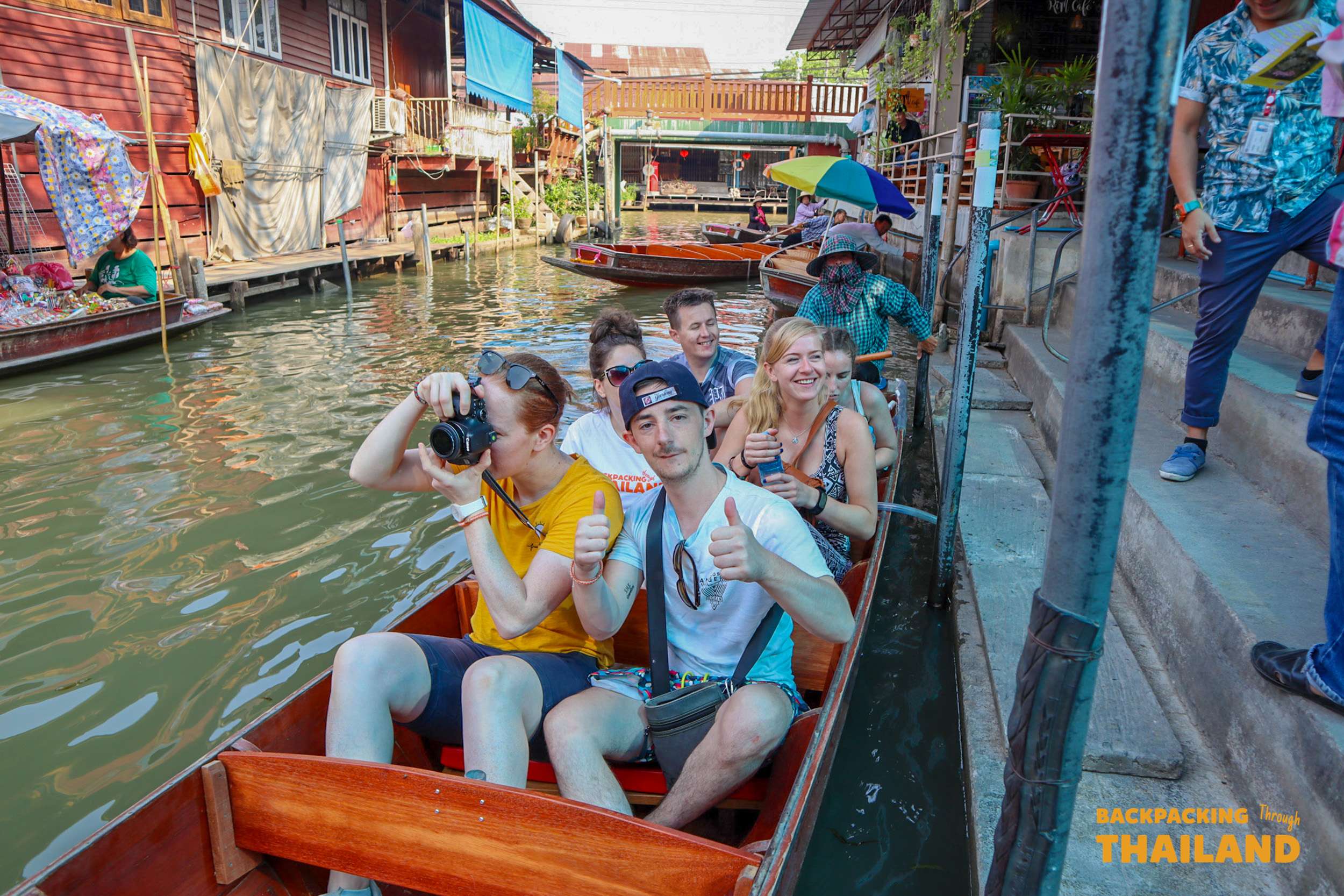 Travelers exploring local culture at Damnoen Saduak market.