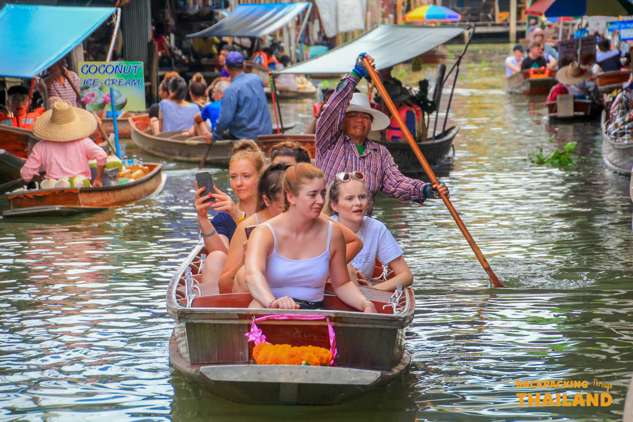 Friends enjoy a lively boat ride through the bustling Amphawa Floating Market in Thailand.