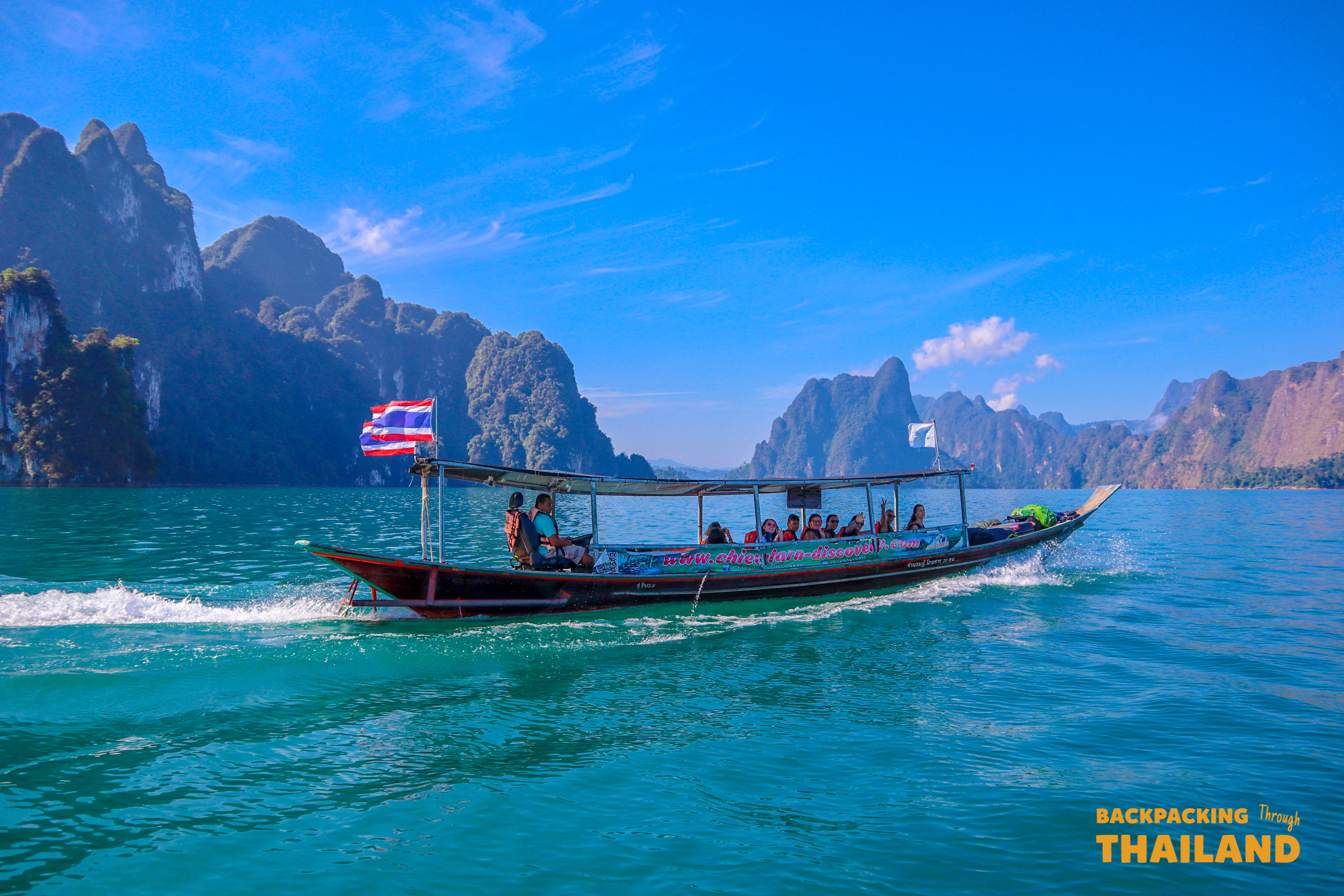 Longtail boat cruising across Khao Sok lake with Thai flag.