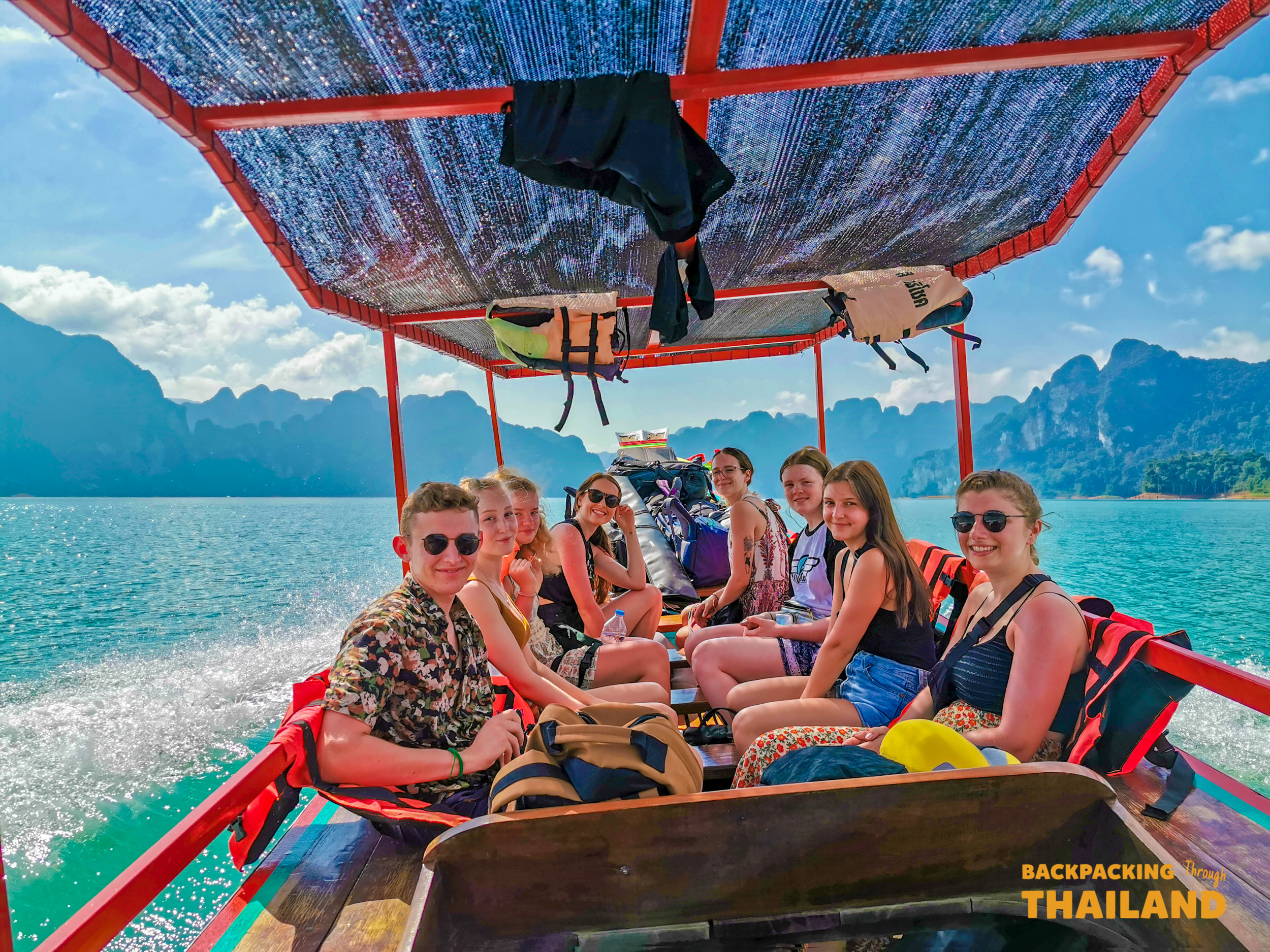 Tour group smiling on longtail boat at Ratchaprapa Dam.