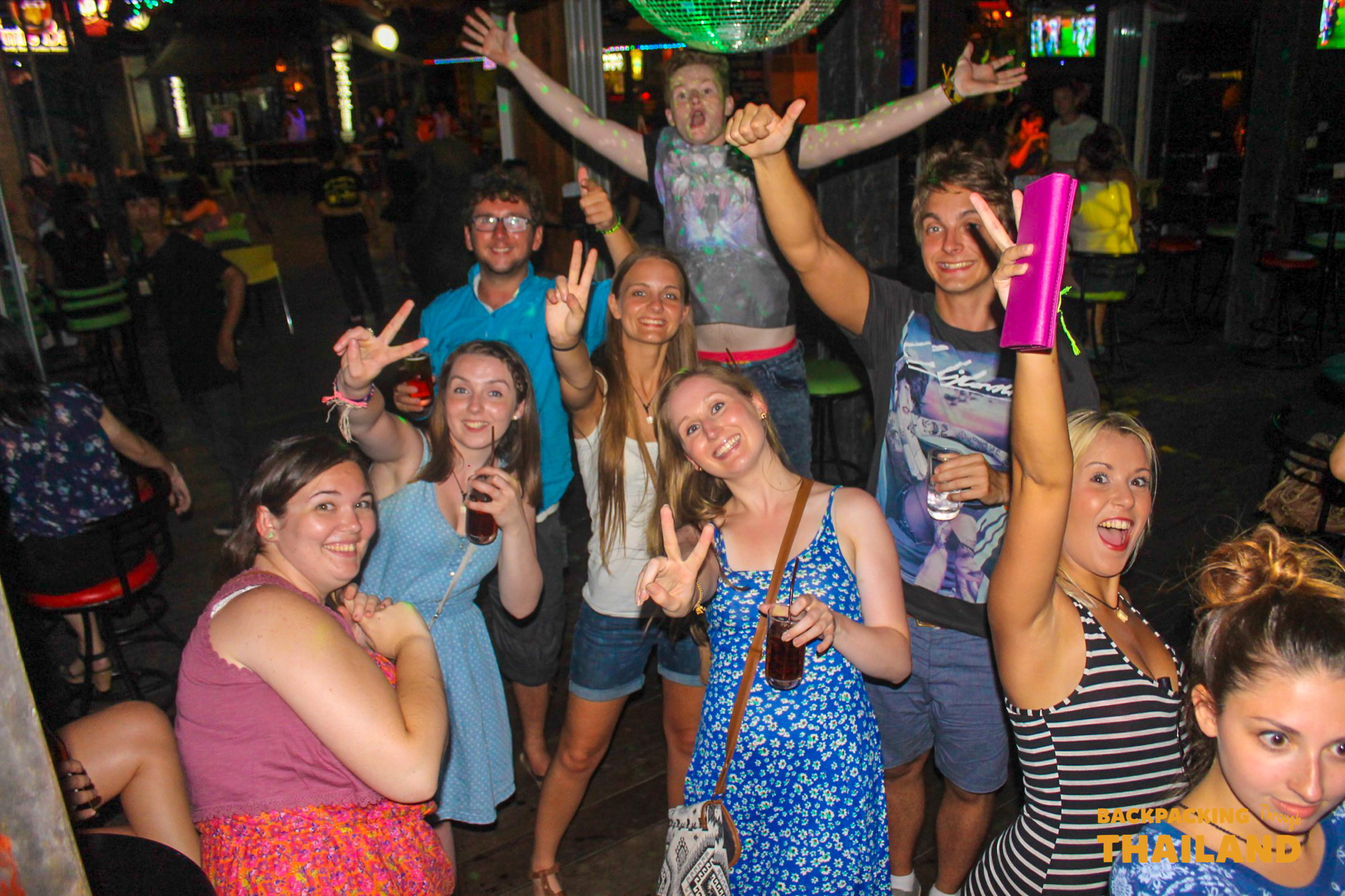 Group of backpackers smiling at nightlife pub in Krabi.