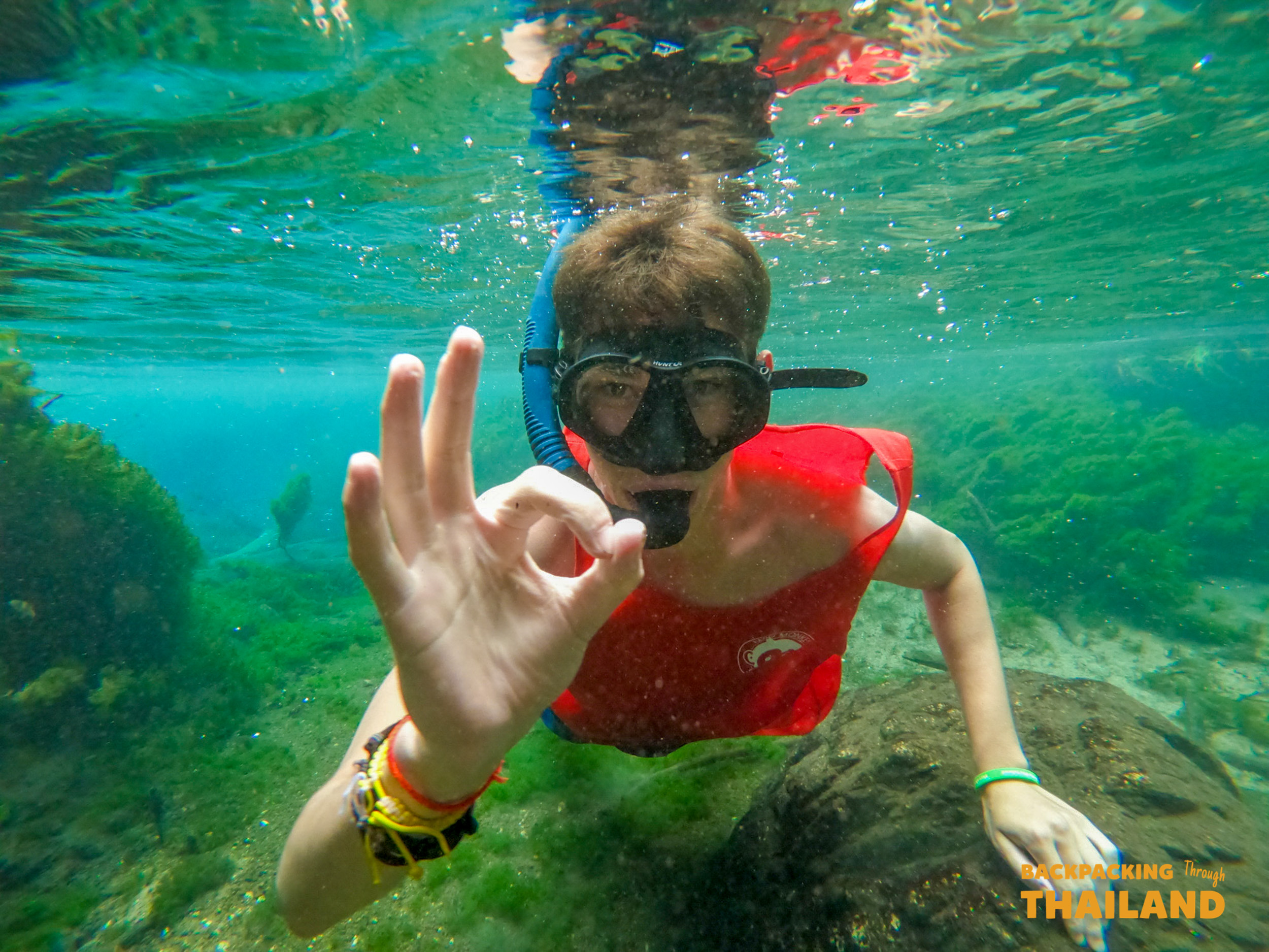 A backpacker gives an OK sign underwater in the crystal-clear emerald waters of Krabi.