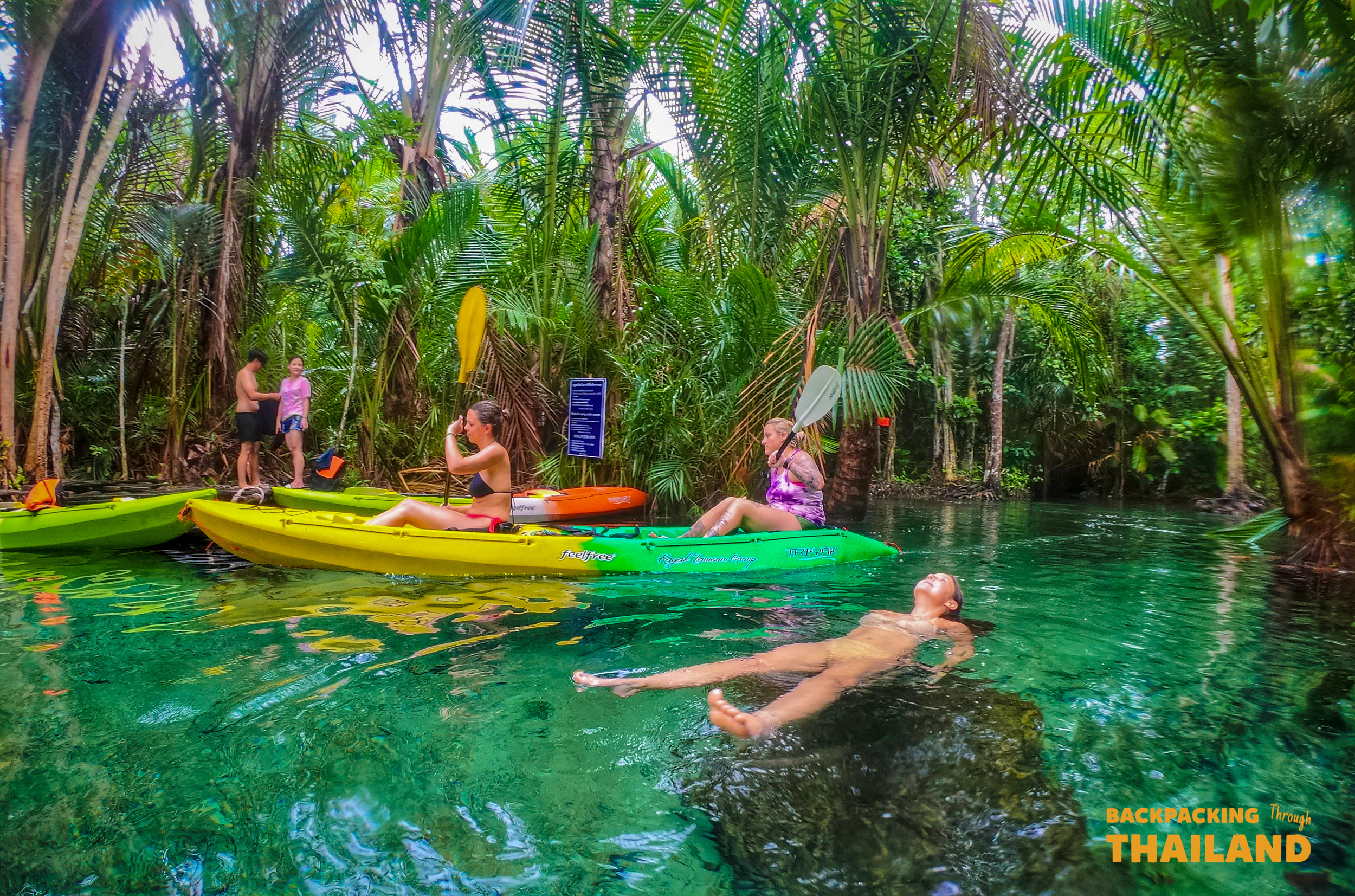 Adventurous travelers kayaking and relaxing in a beautiful clear turquoise jungle pool in Thailand.