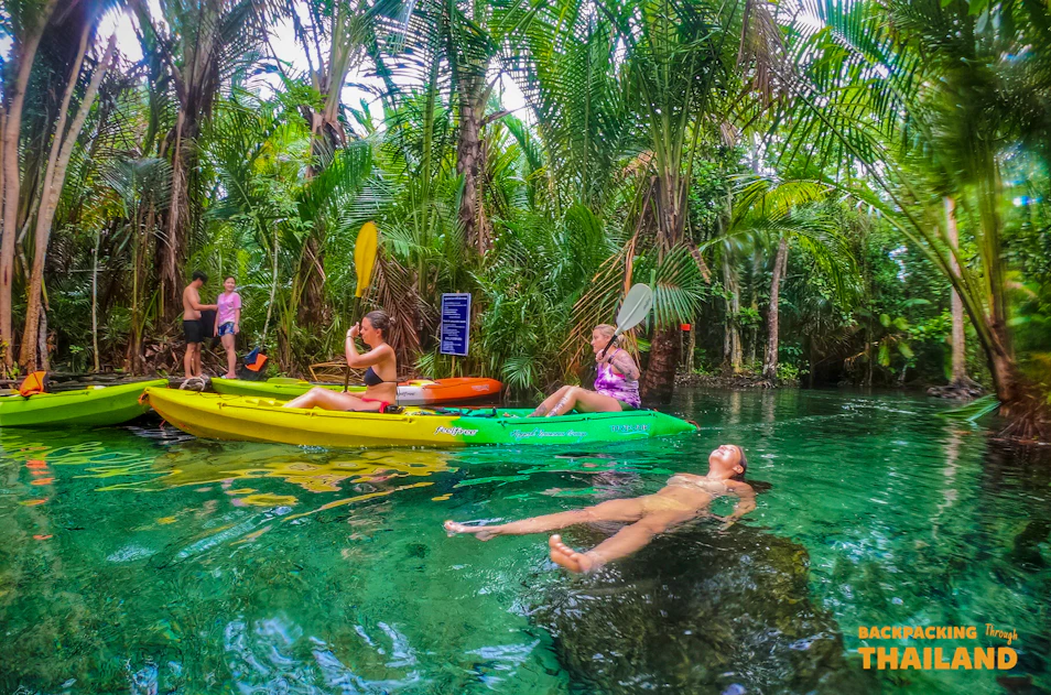 Adventurous travelers kayaking and relaxing in a beautiful clear turquoise jungle pool in Thailand.