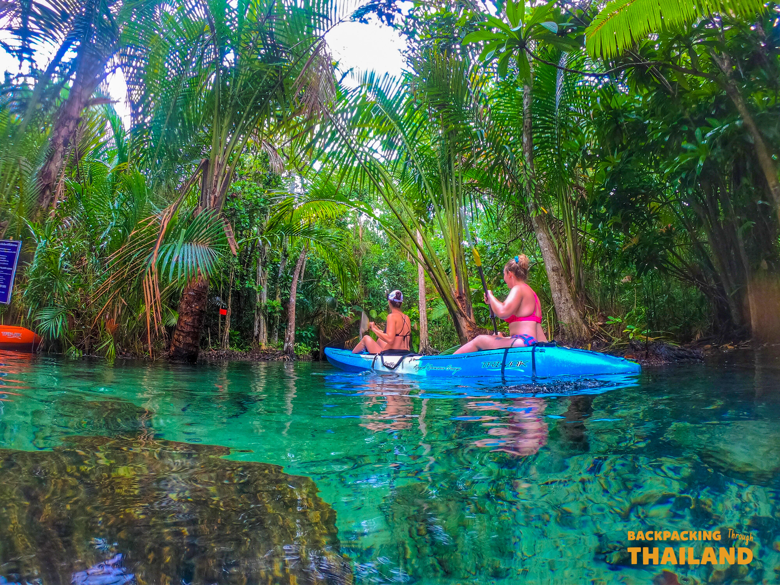 Two people kayaking on crystal-clear emerald water surrounded by lush tropical jungle in Krabi.