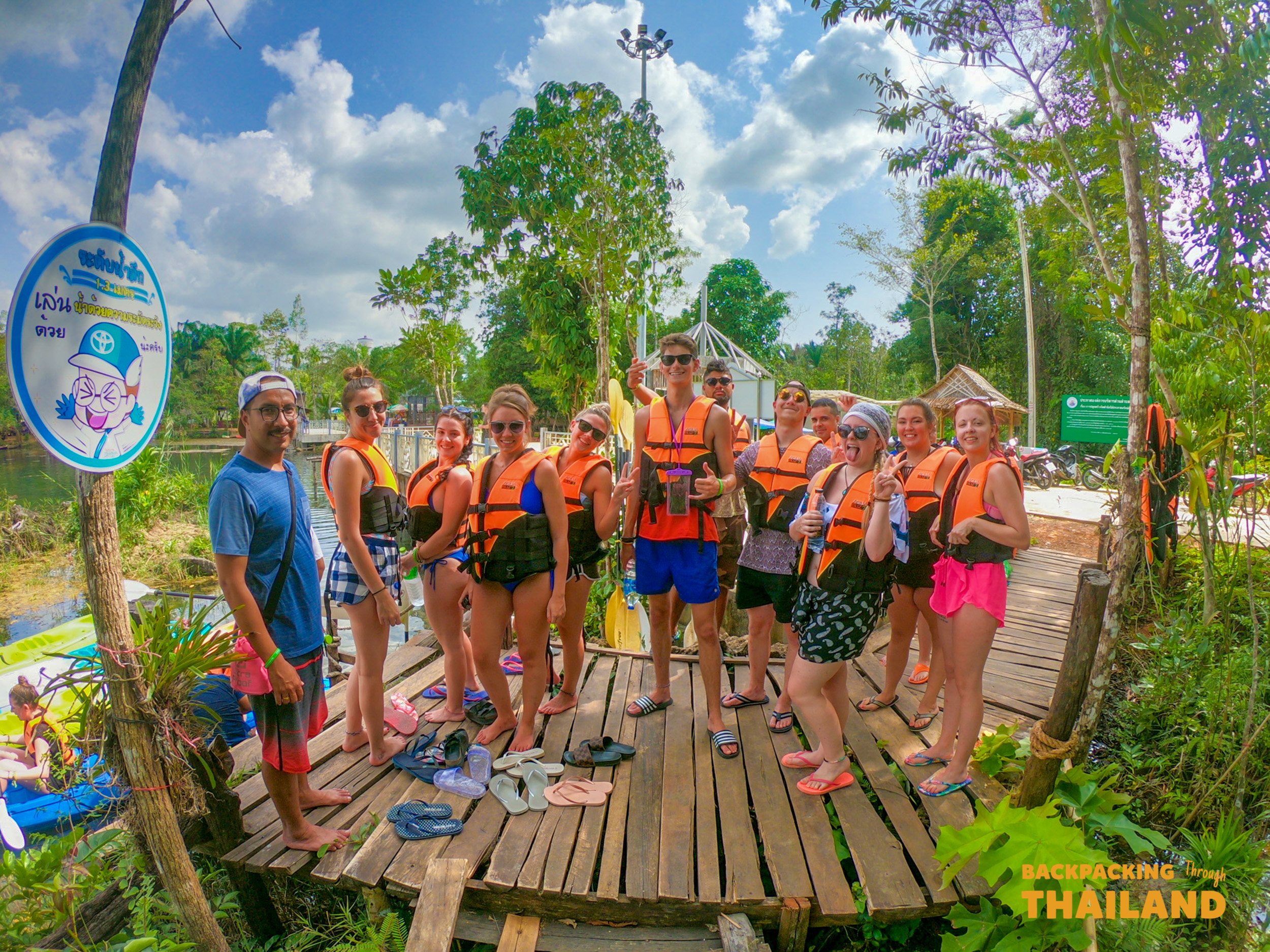 A group of happy backpackers in life vests ready for a mangrove kayak adventure in Krabi, Thailand.