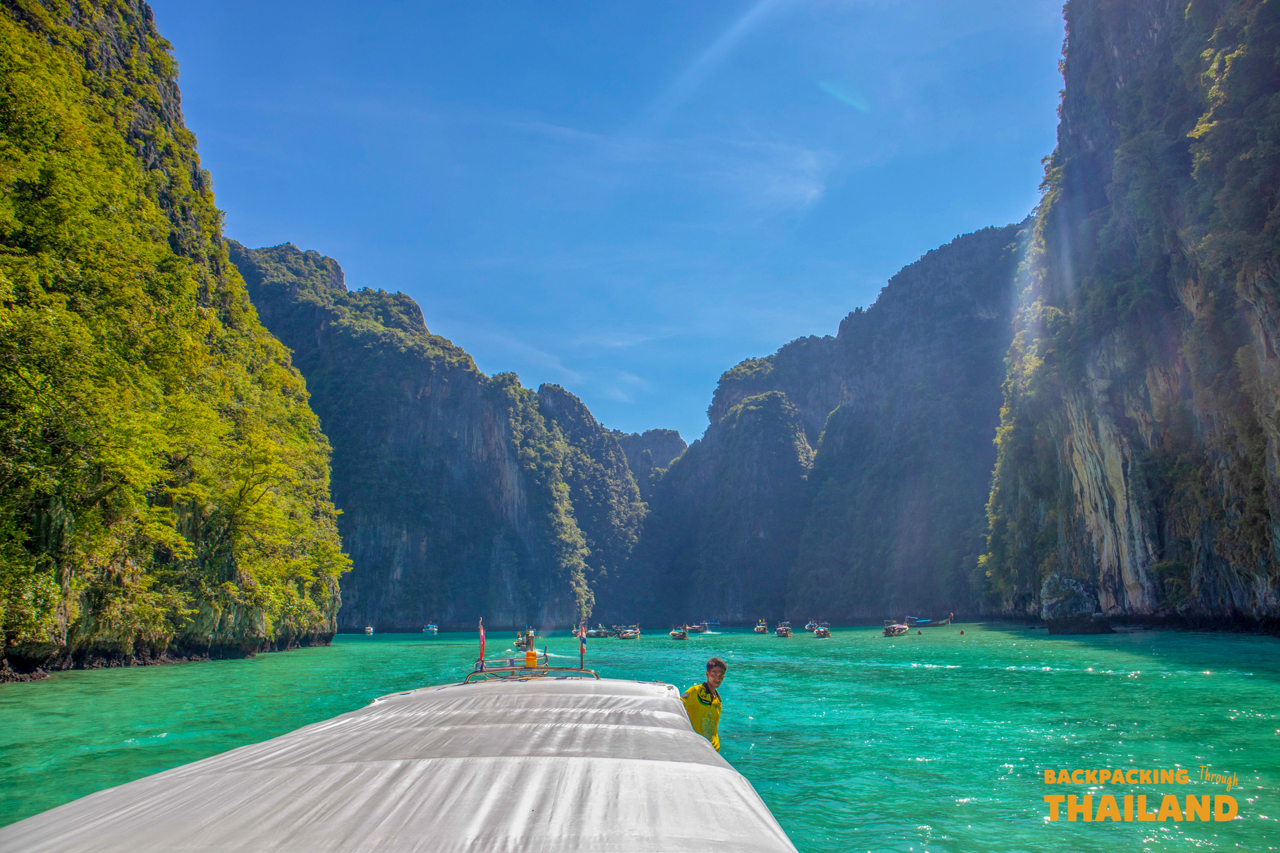 A boat approaches Maya Bay, surrounded by towering limestone cliffs and turquoise water under a clear sky.
