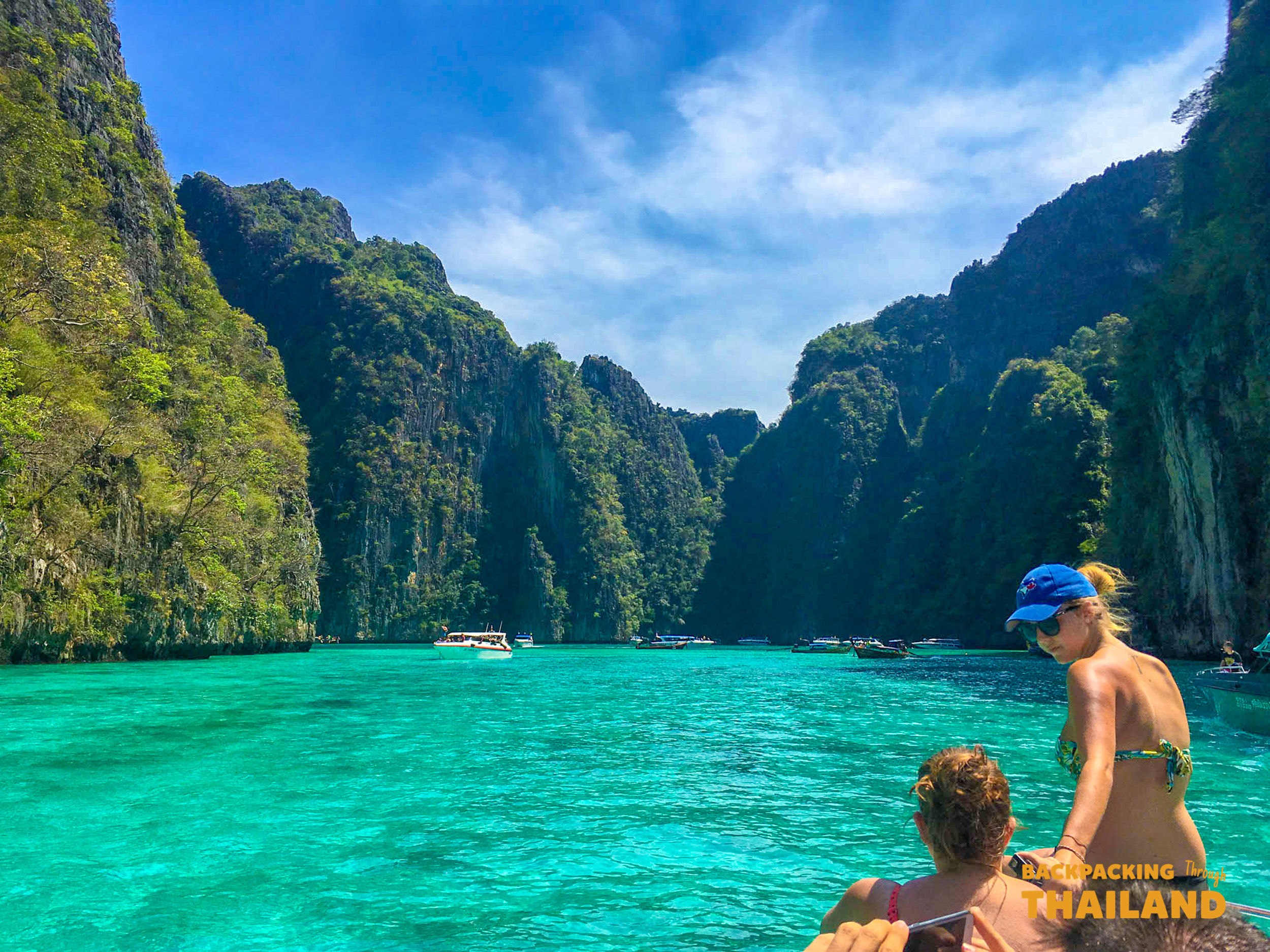 Travelers on a boat in Thailand's Phi Phi Islands, admiring the turquoise water and towering limestone cliffs.