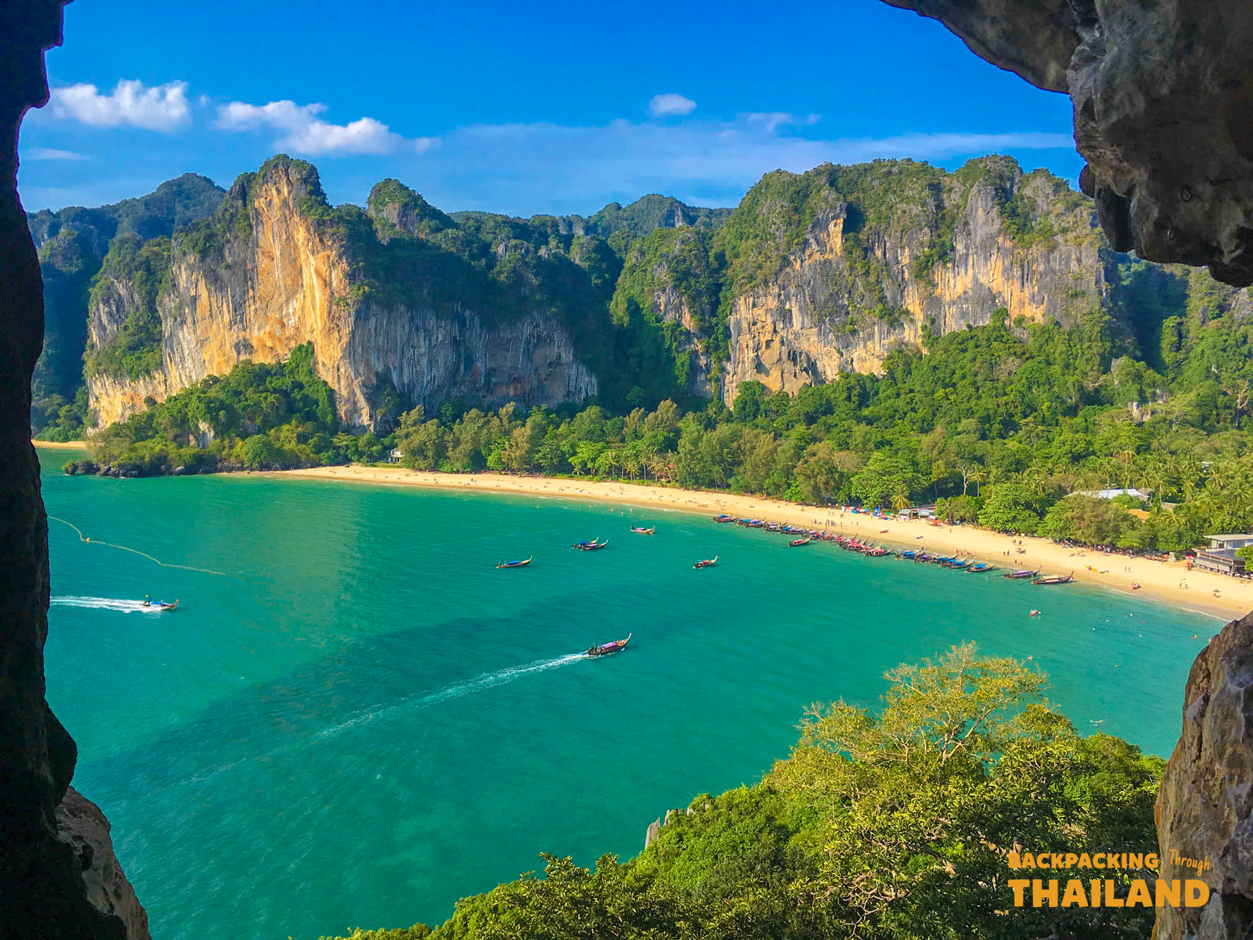 Longtail boats cruise the turquoise waters of Railay Beach, Krabi, surrounded by dramatic limestone cliffs.
