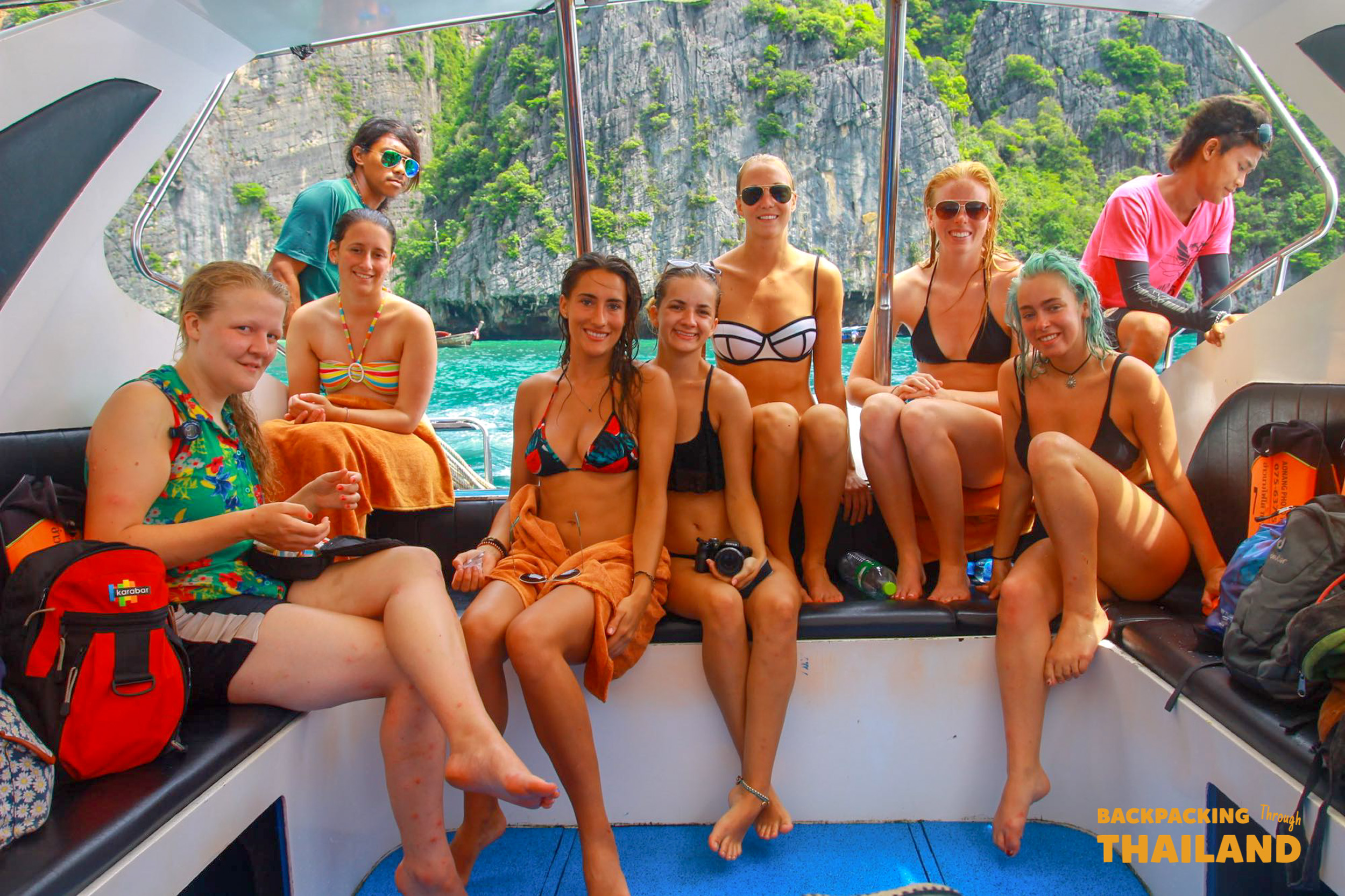 A group of happy backpackers enjoy a boat trip among the stunning limestone cliffs of Koh Phi Phi, Thailand.