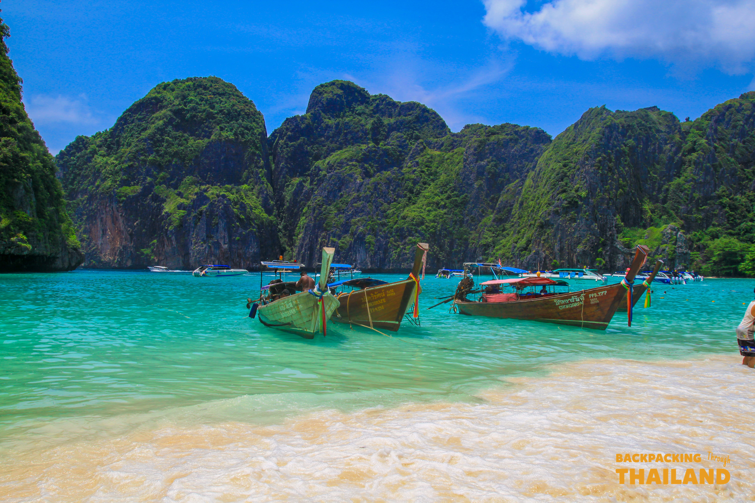 Traditional longtail boats on the pristine white sand beach of Koh Phi Phi, surrounded by turquoise water.