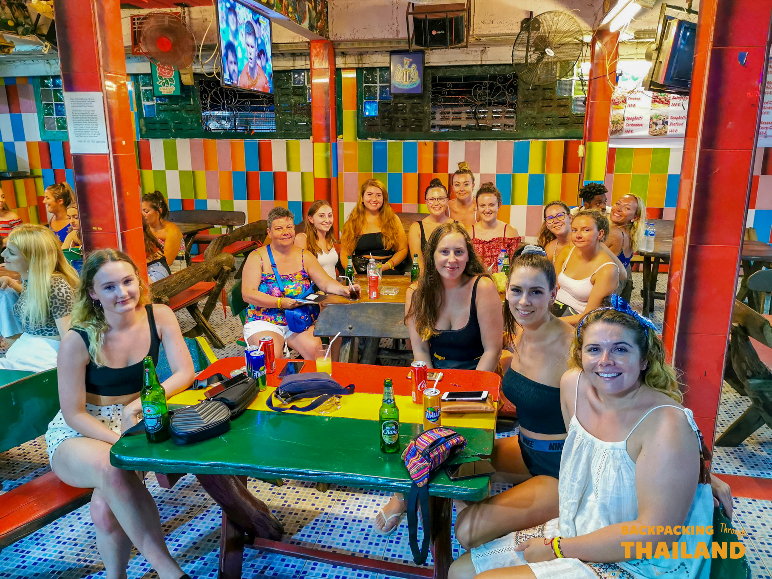 Smiling backpackers socialize over drinks at a vibrant bar in Phuket, Thailand.