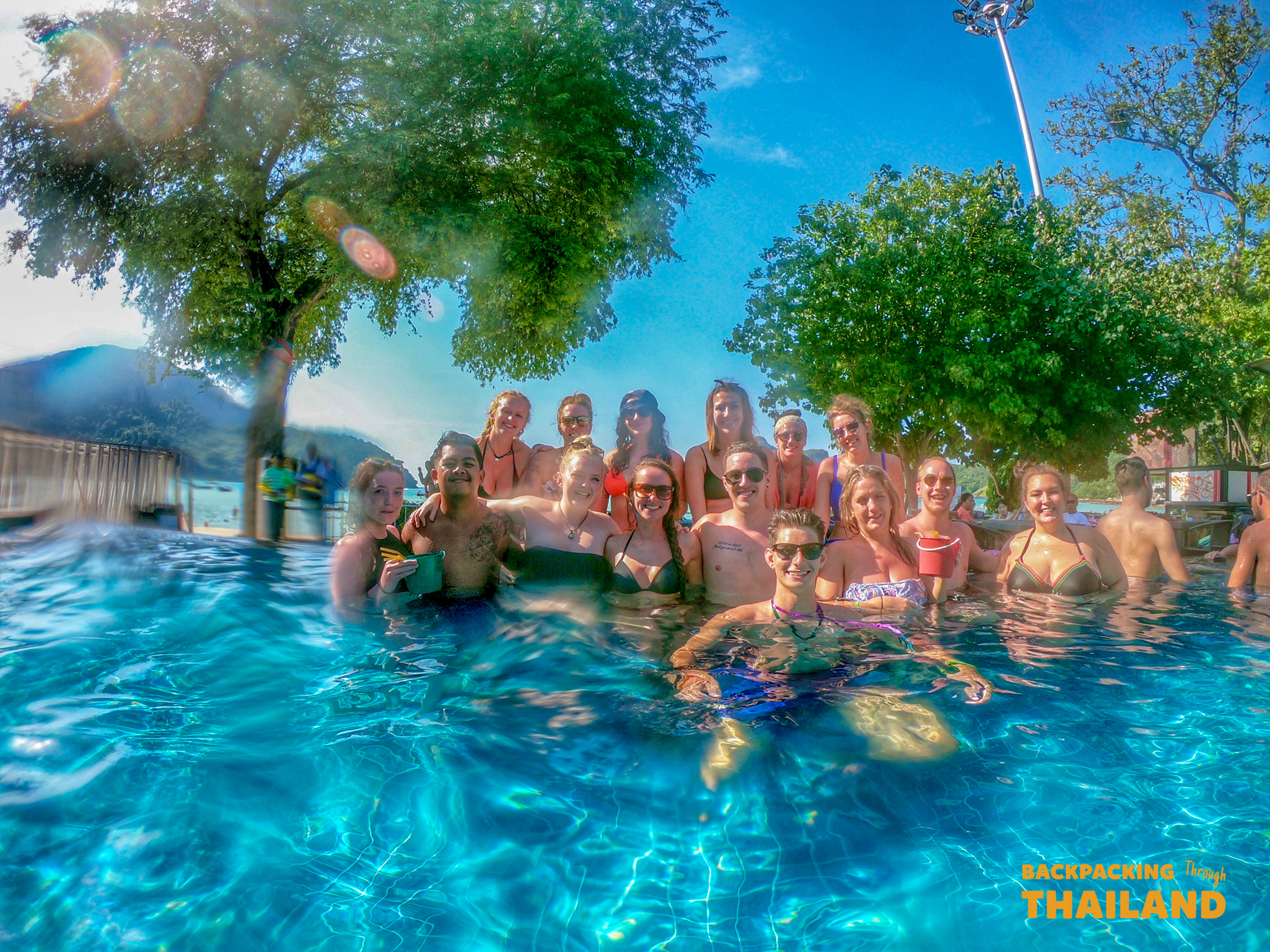Happy backpackers enjoying a refreshing swim in a tropical pool overlooking the ocean in Thailand.