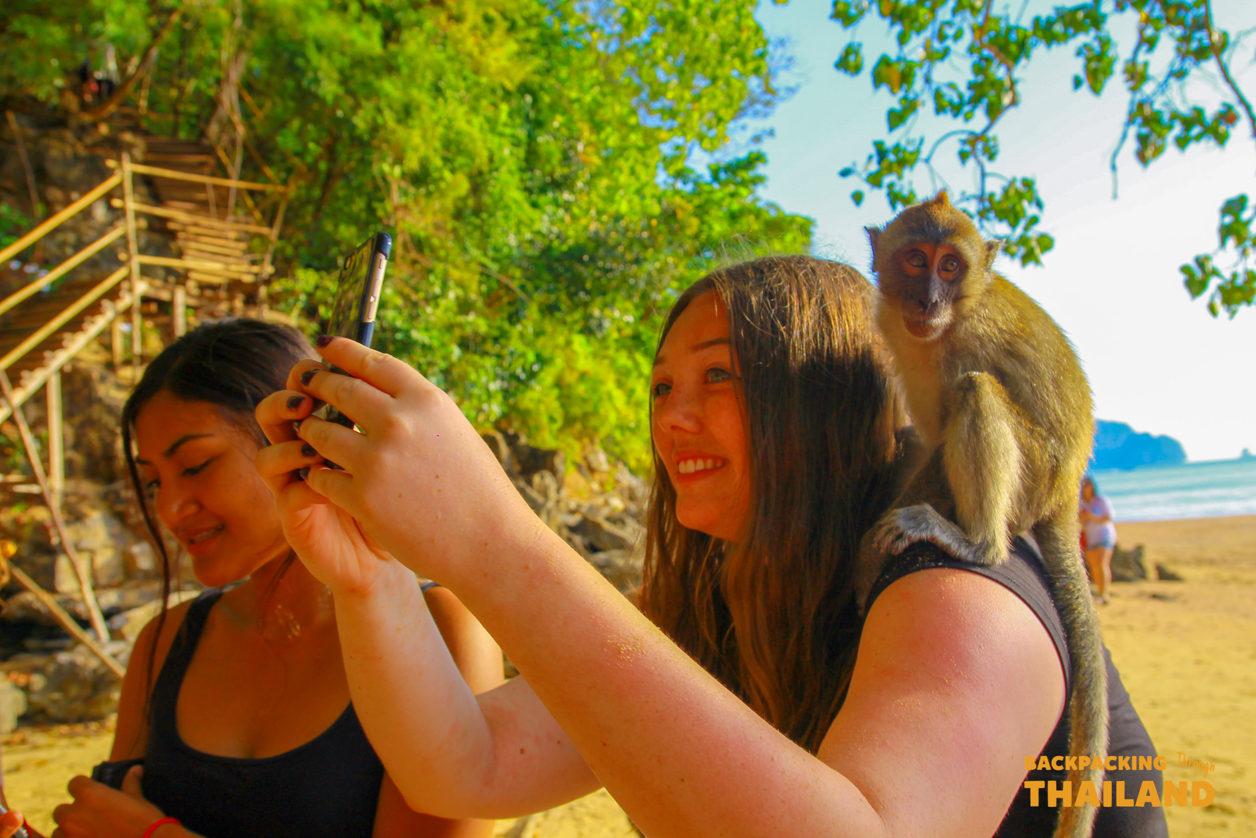 A happy woman smiles as a monkey sits on her shoulder at Railay Beach, Thailand.