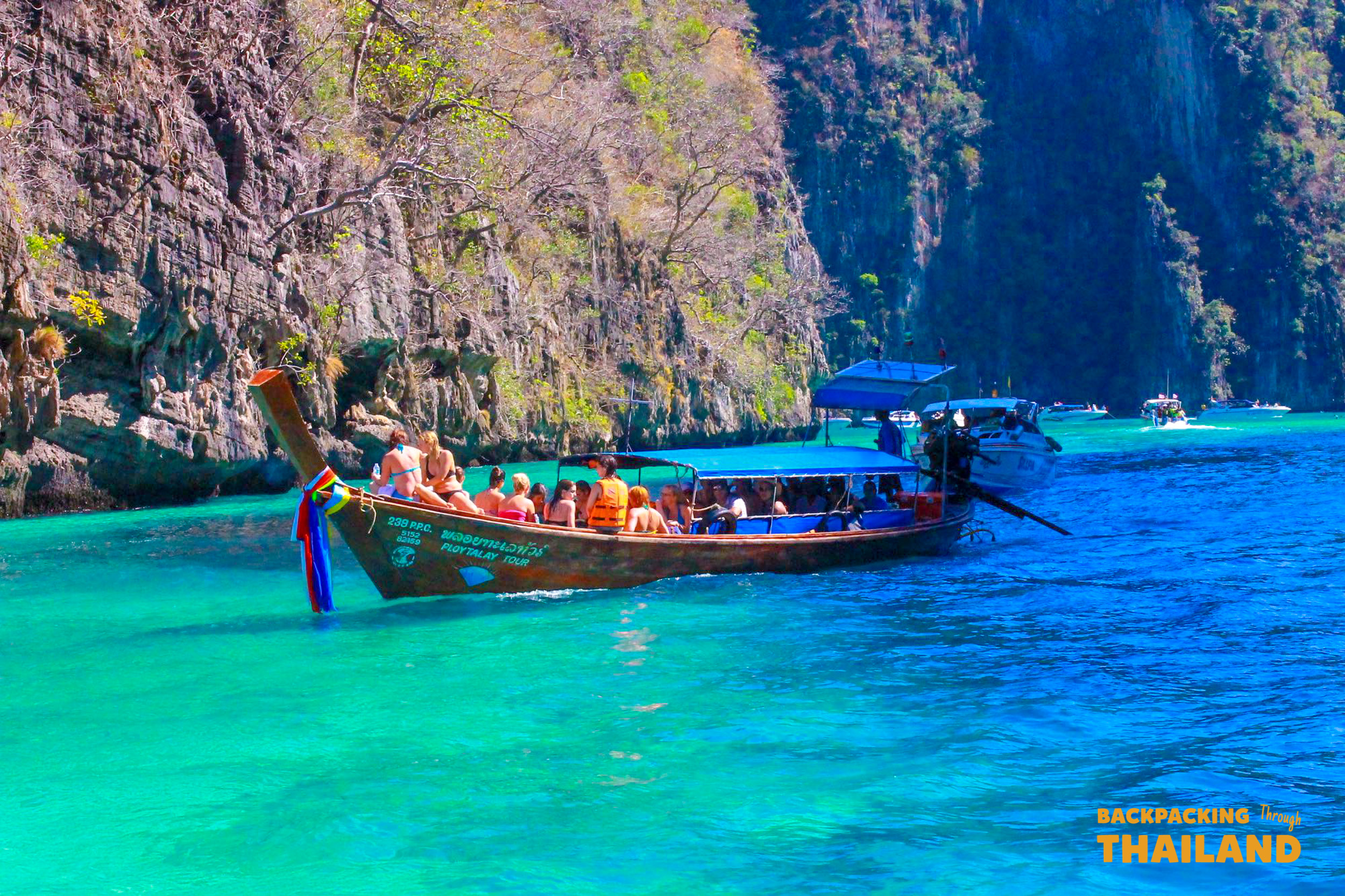 Tourists on a longtail boat cruise past towering limestone cliffs in the clear turquoise waters of Krabi.