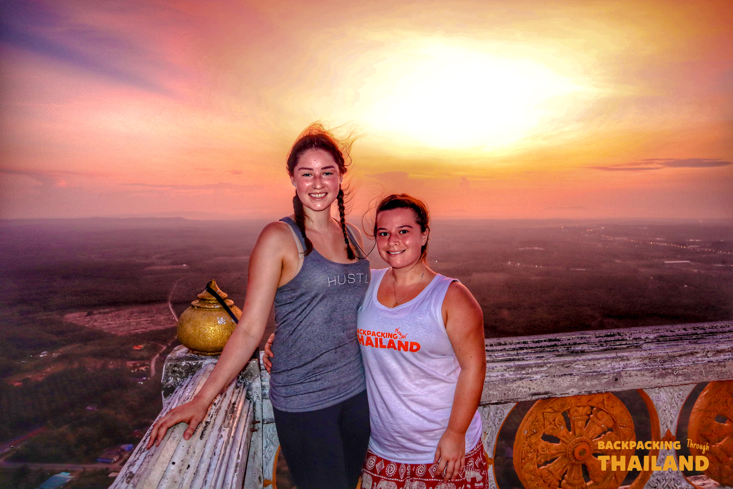 Two smiling women enjoy a breathtaking sunset view from Tiger Cave Temple in Krabi.