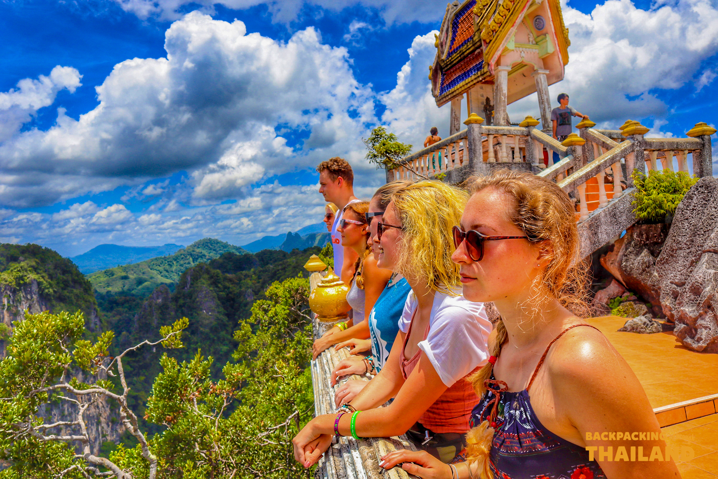 Backpackers admire the breathtaking views of green mountains and valleys from a temple viewpoint in Krabi, Thailand.