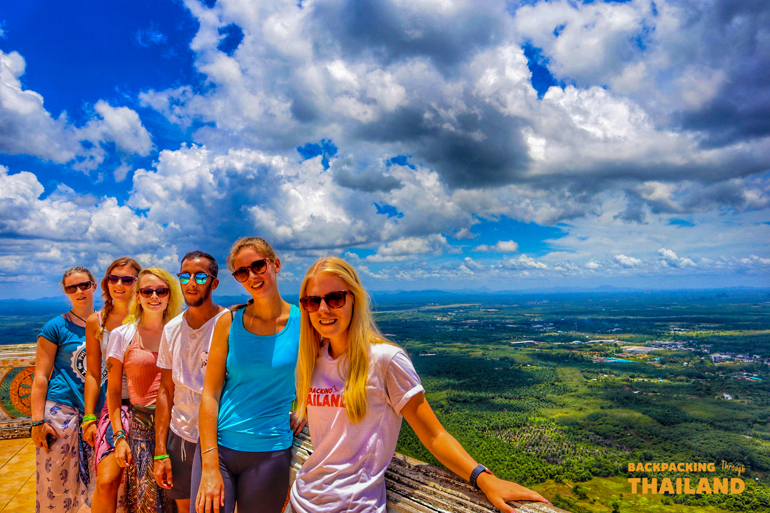 Six happy backpackers pose at the summit of Tiger Cave Temple, enjoying the stunning Krabi view.