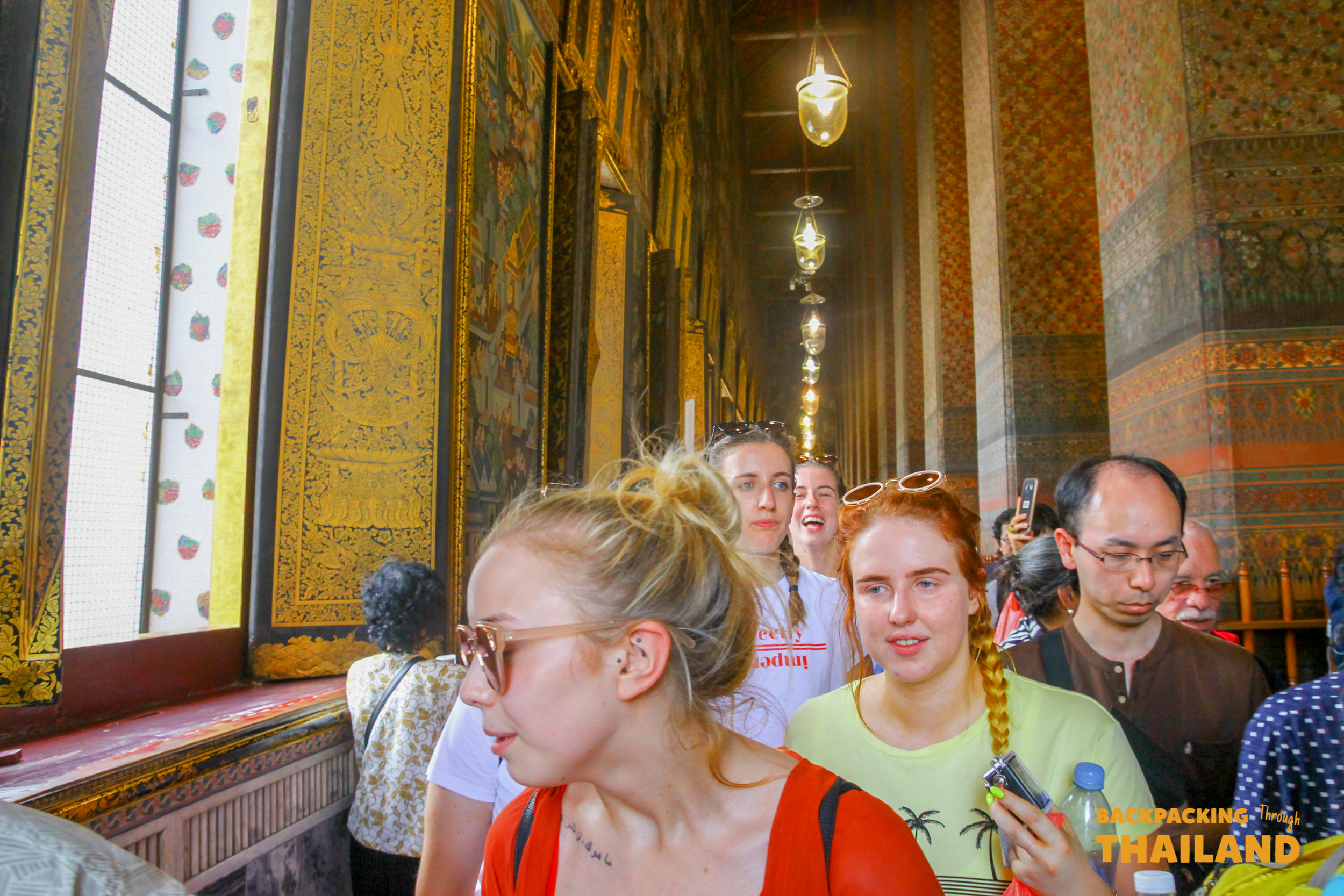A group of backpackers walks through a stunning golden temple corridor, admiring the intricate details in Bangkok.