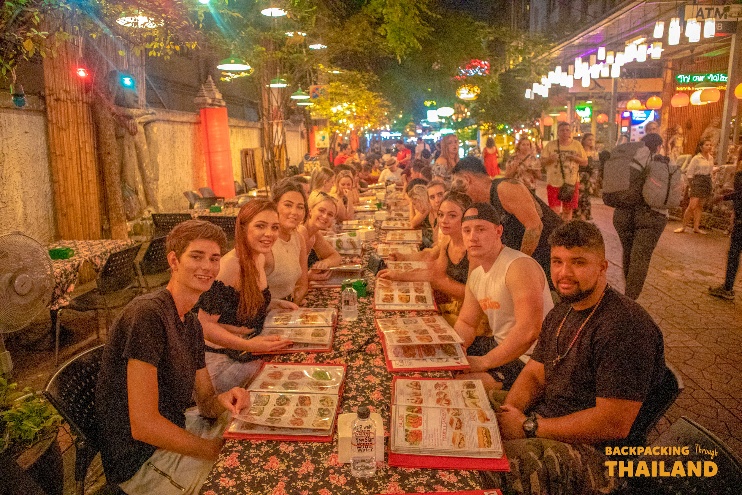 Young travelers share a fun group dinner at a bustling outdoor restaurant in Bangkok.