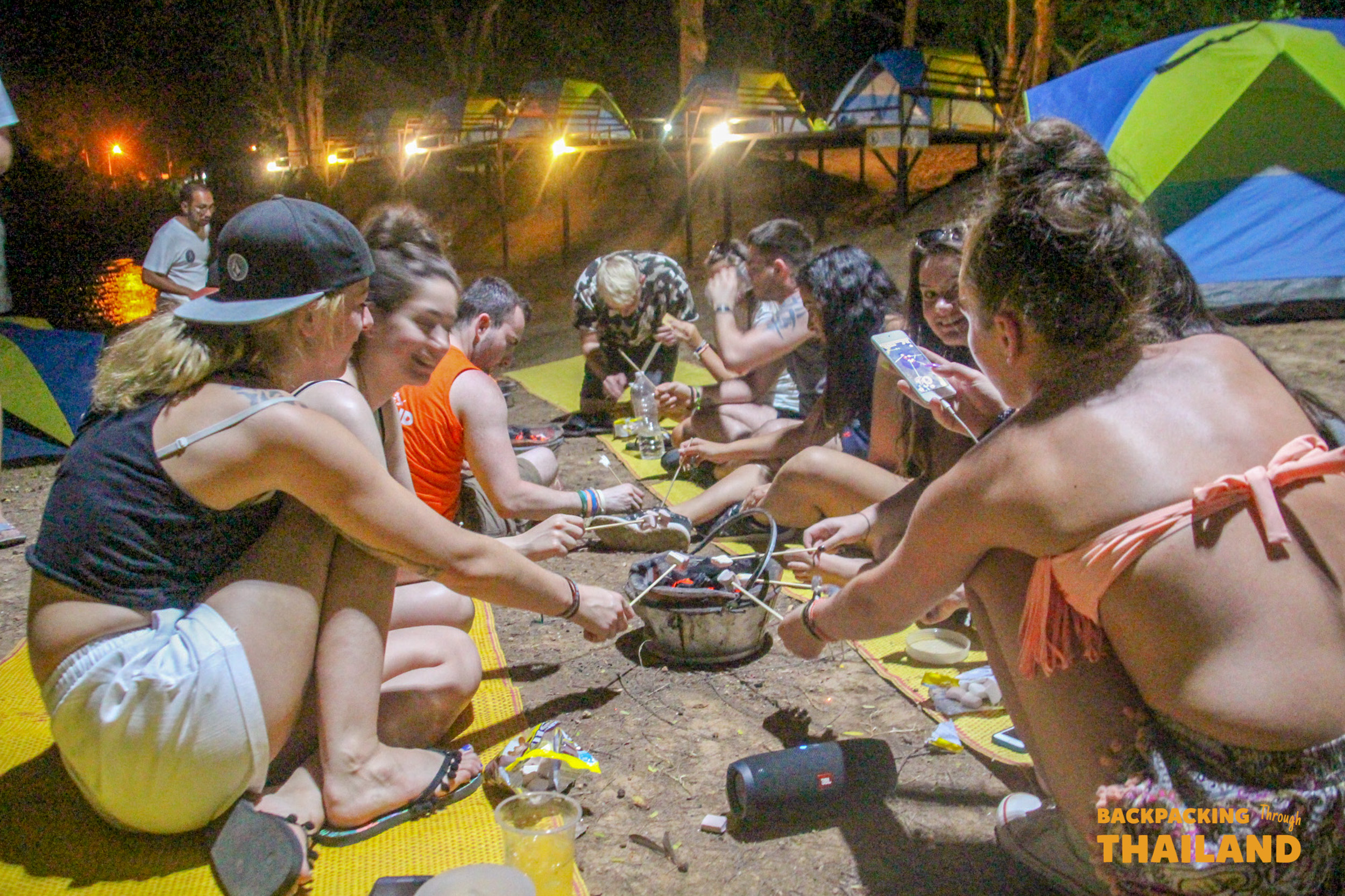 Young backpackers enjoying a fun night roasting marshmallows at a lively campsite in Erawan National Park.