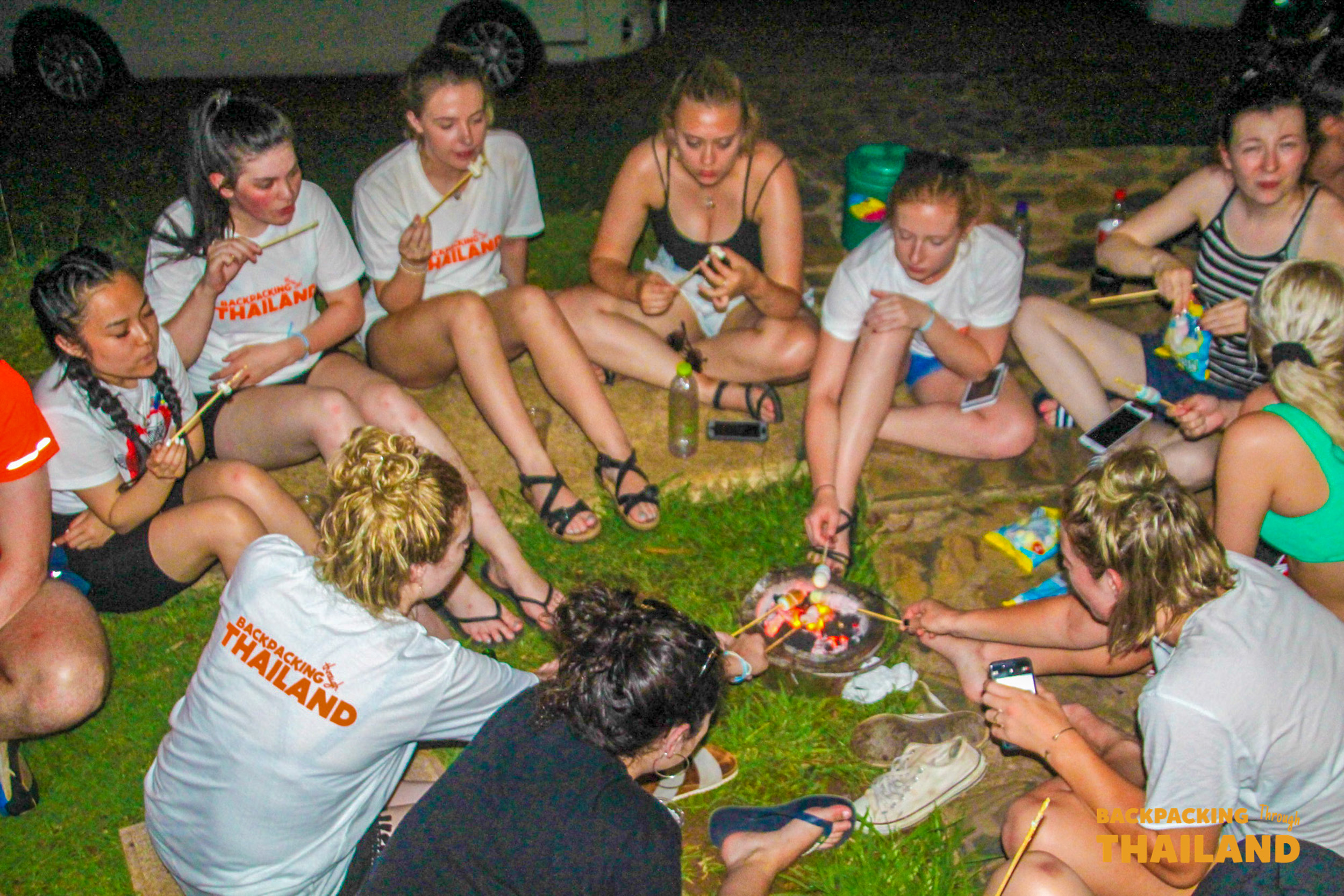 Backpackers gather around a campfire, roasting marshmallows and enjoying a social evening at Erawan National Park.
