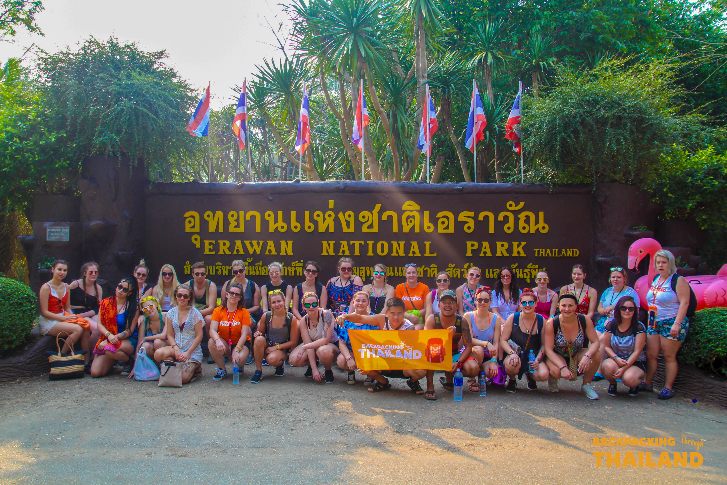 Happy backpackers gather at the Erawan National Park entrance, ready to explore the waterfalls and jungle.