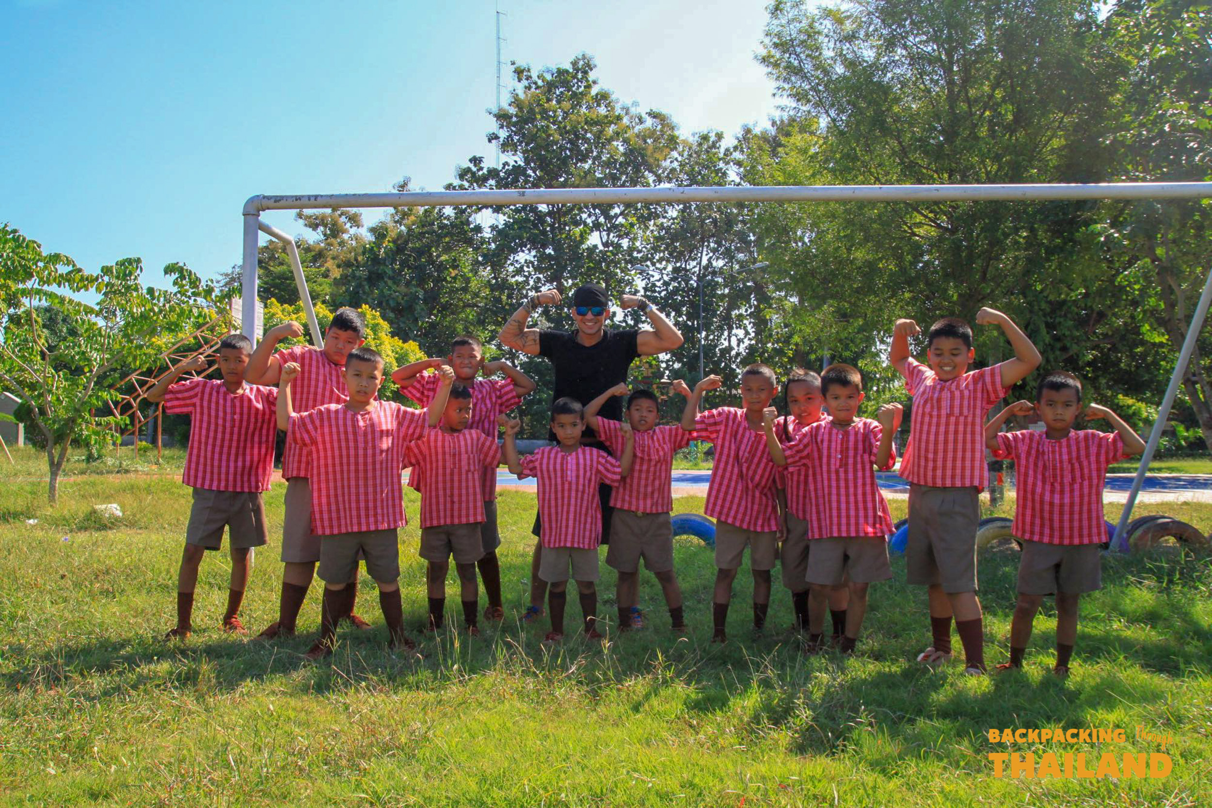 Smiling Thai schoolboys and a guide playfully flex their muscles at a local school.