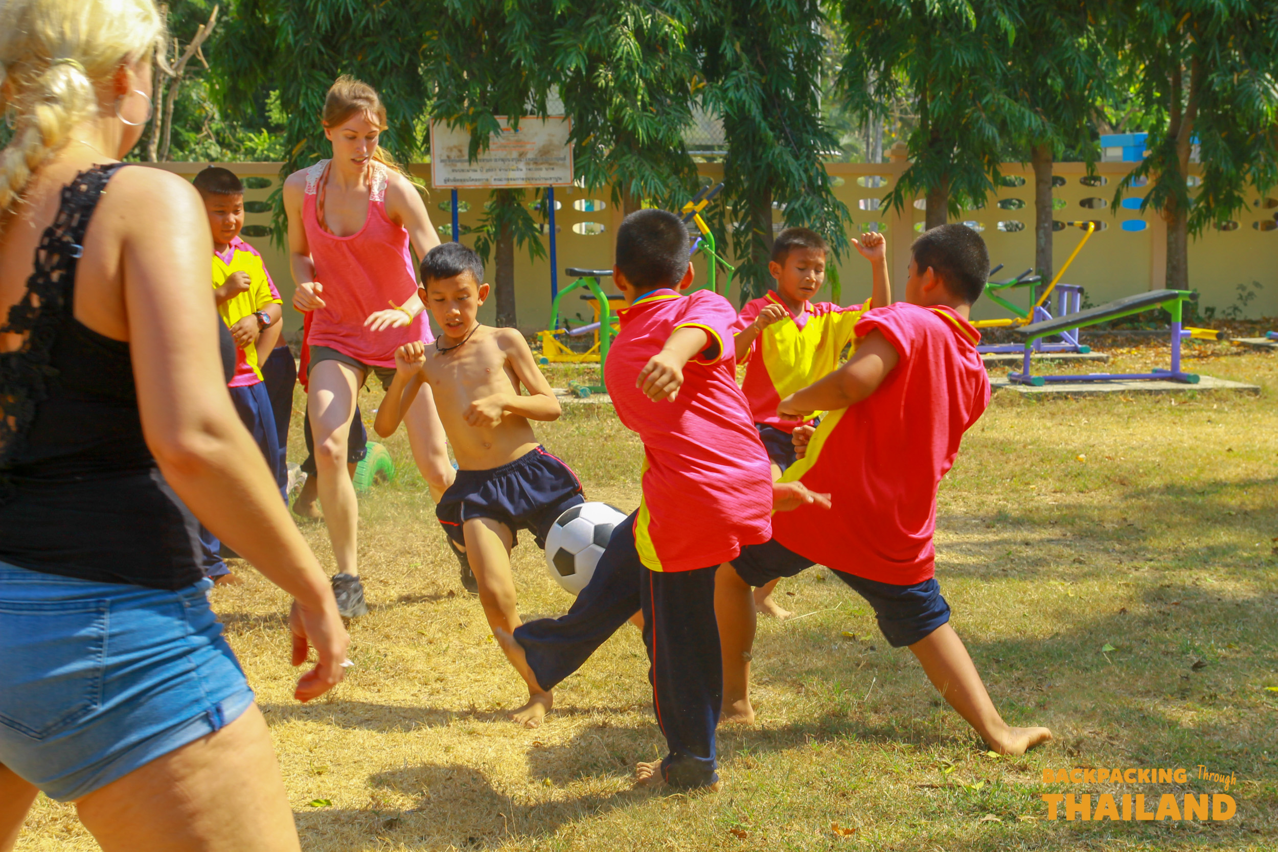 Travelers enjoy a fun game of football with children during a school visit in Thailand.
