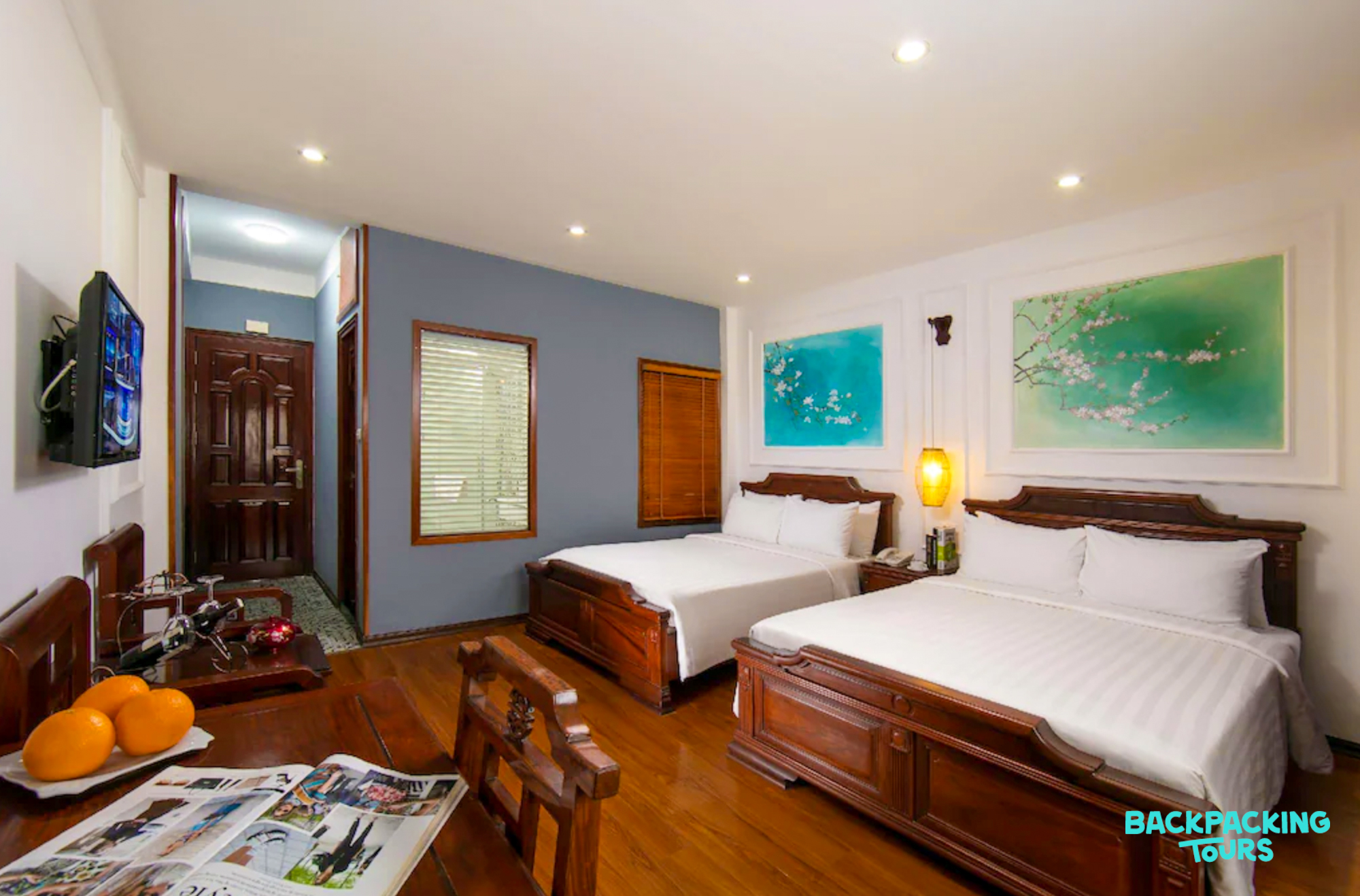 A cozy hotel room in Hanoi with two beds, a wooden desk, and vibrant abstract art.