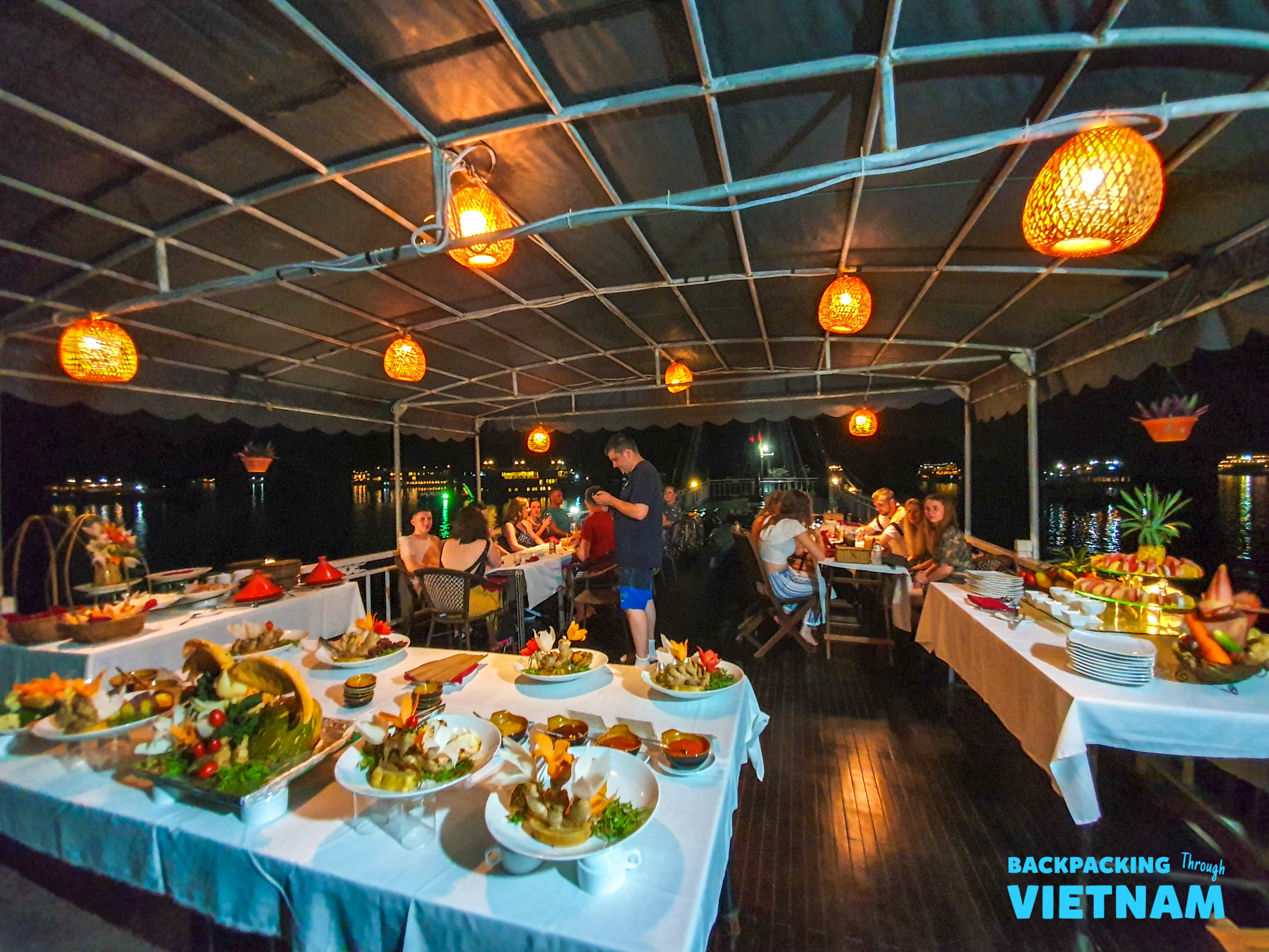 Guests enjoy a delicious buffet dinner under warm lanterns on a boat in Halong Bay.