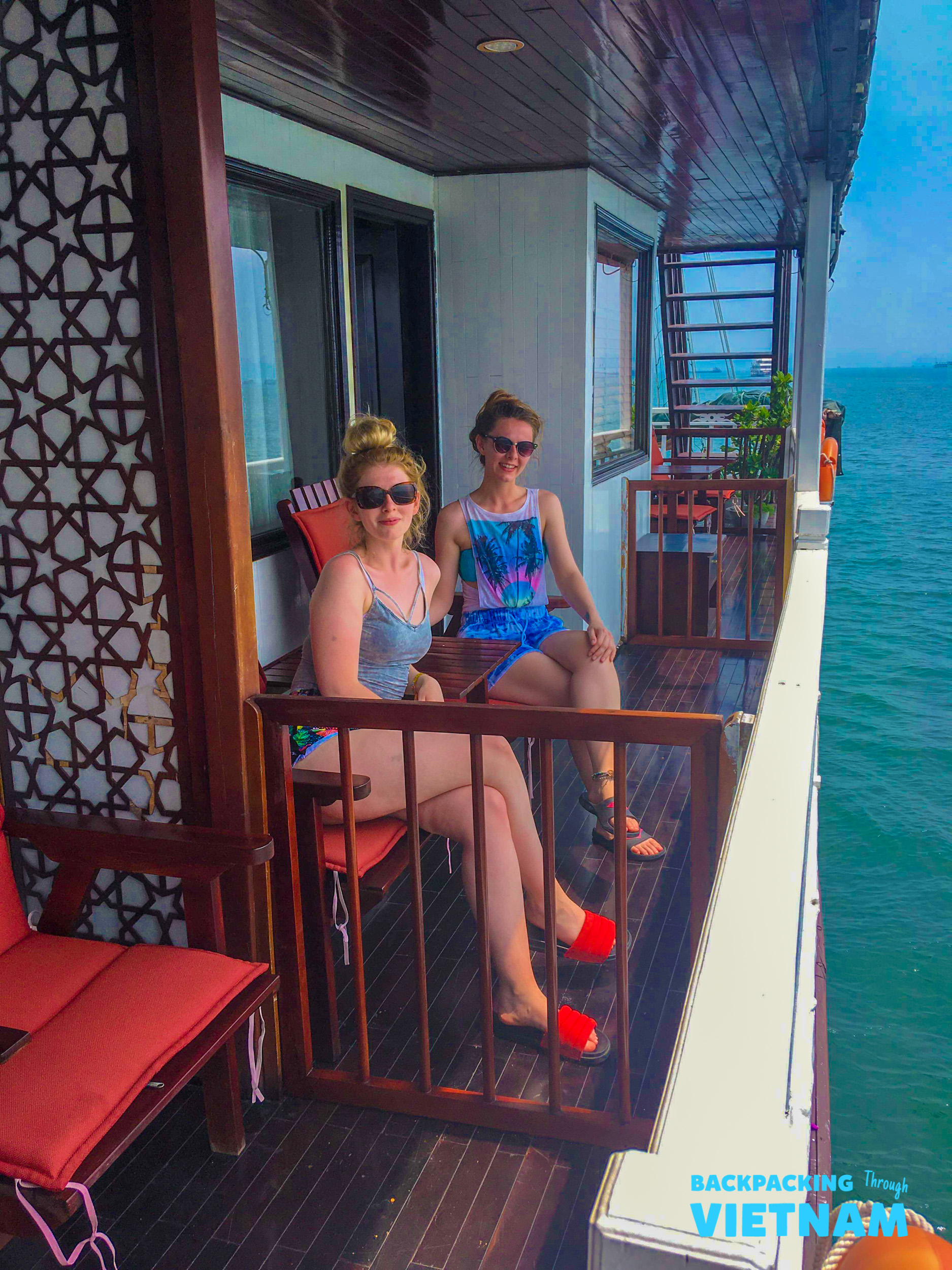 Two women relax on a boat balcony overlooking the beautiful waters of Halong Bay, Vietnam.