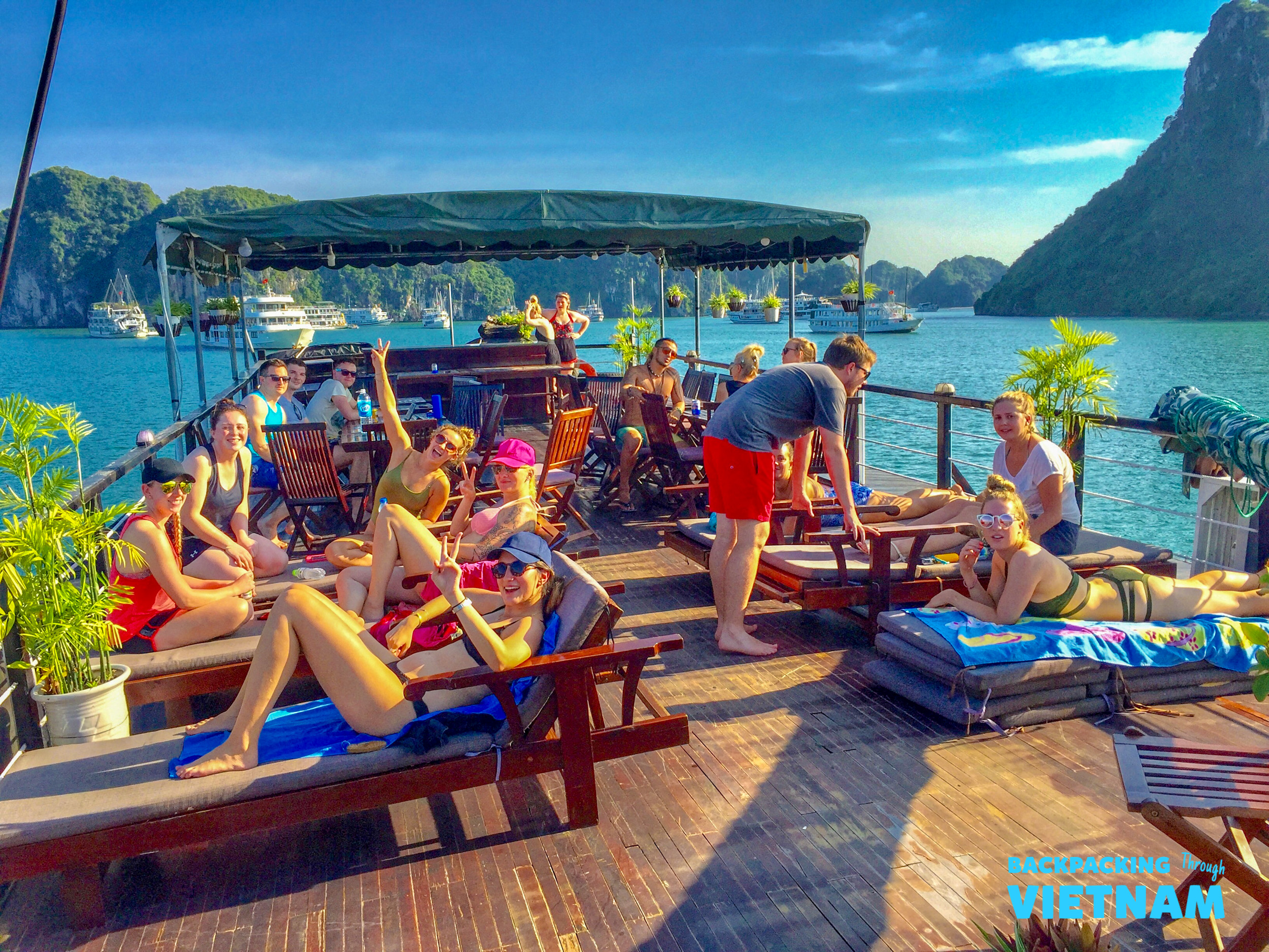 Travelers relax on a boat deck, enjoying the sunset and limestone karsts of Halong Bay, Vietnam.