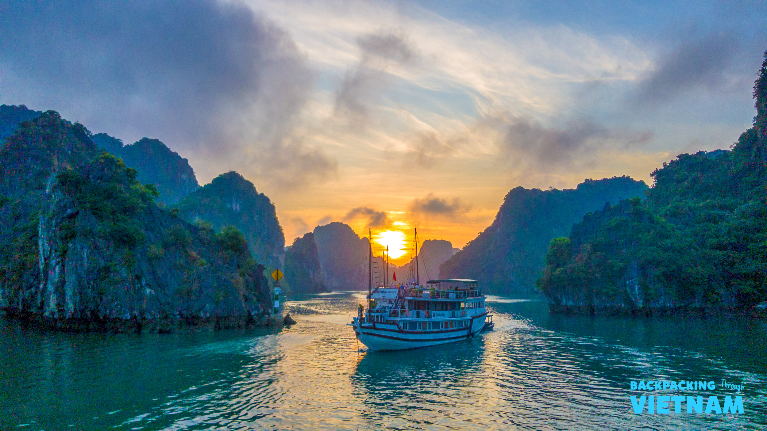 A cruise boat sails through Halong Bay's majestic limestone karsts at a breathtaking sunset.