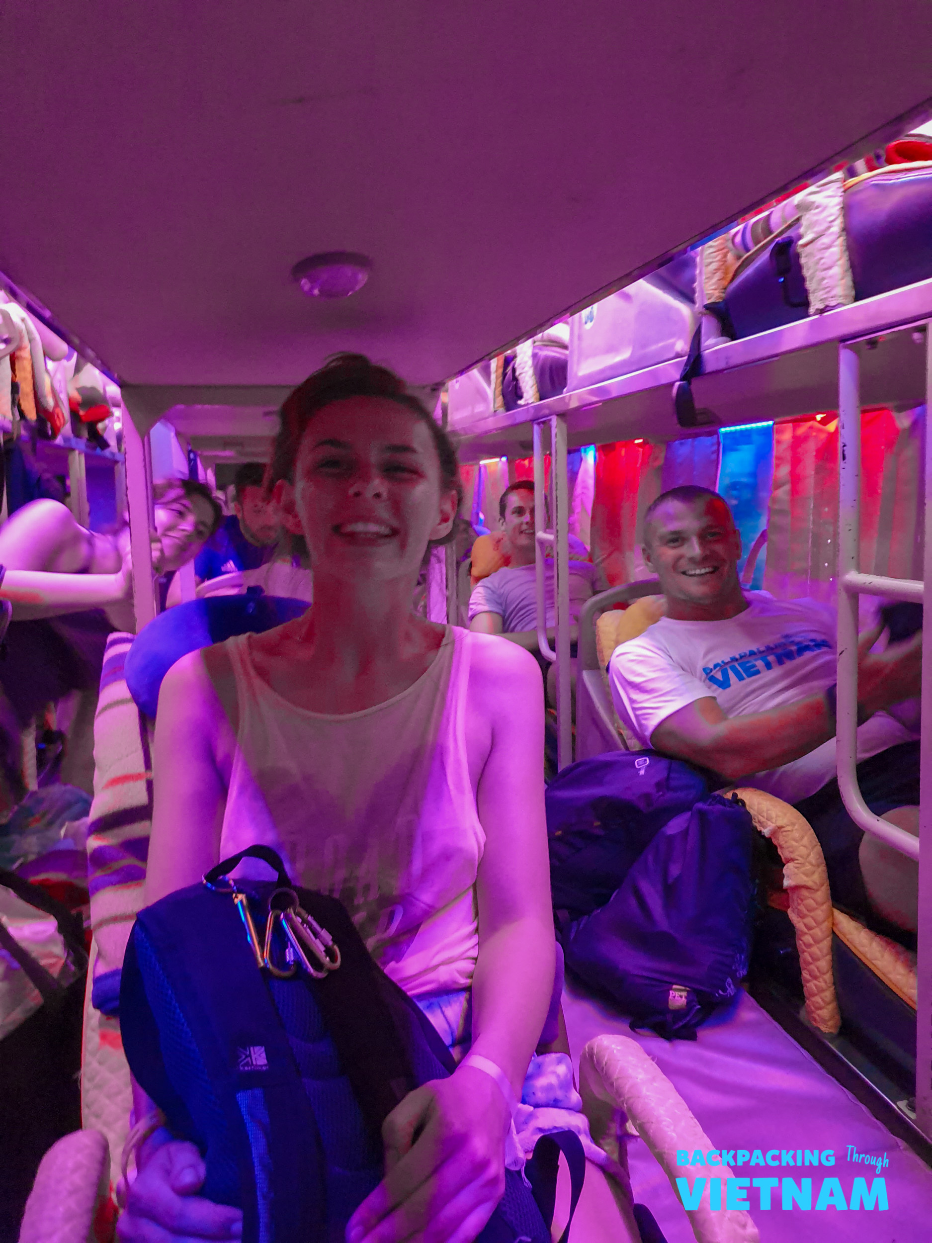 Smiling backpackers enjoy a vibrant purple-lit sleeper bus journey through Vietnam.