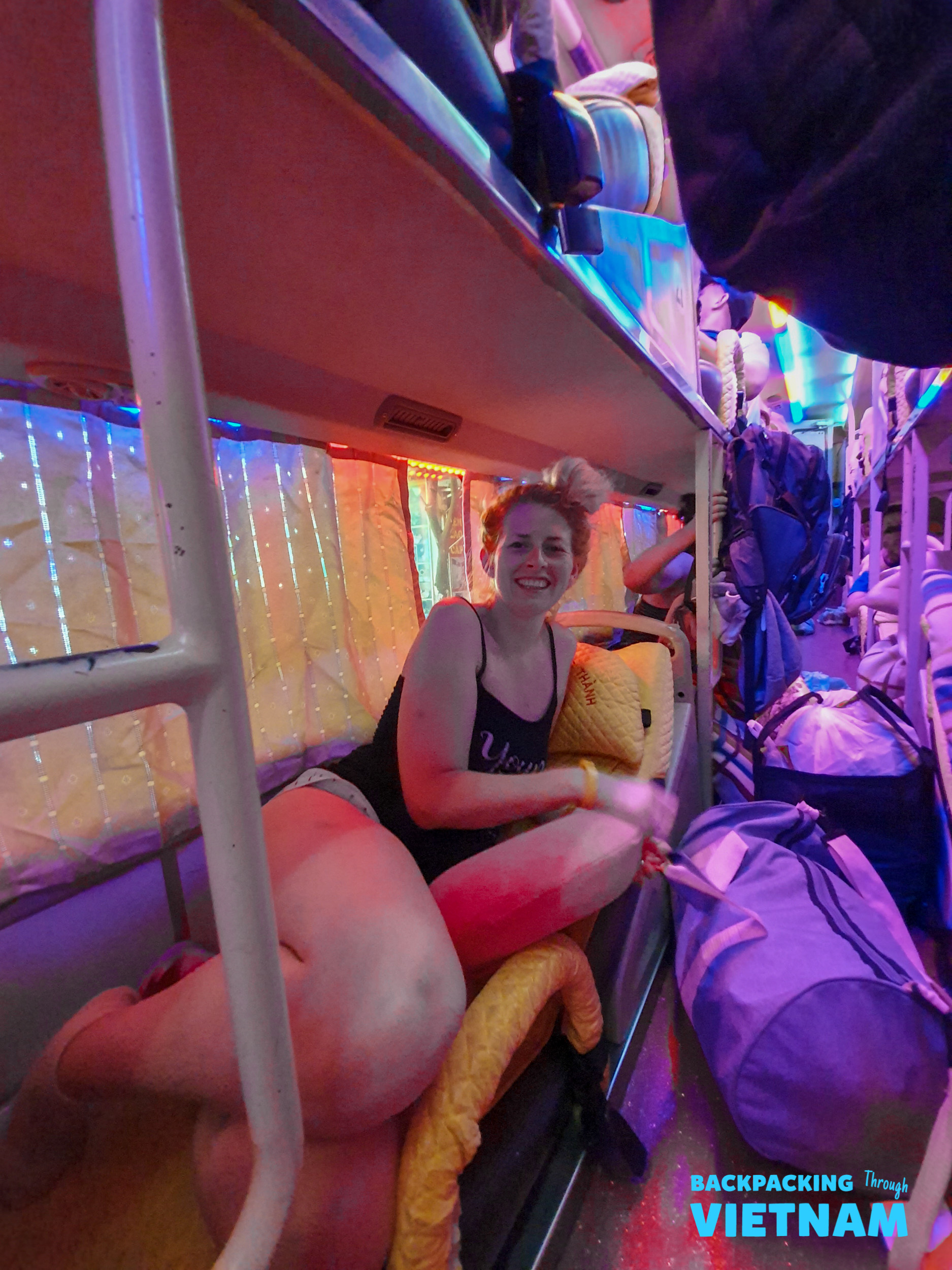 A smiling woman relaxes in a brightly lit sleeper bus bunk during her Vietnam adventure.