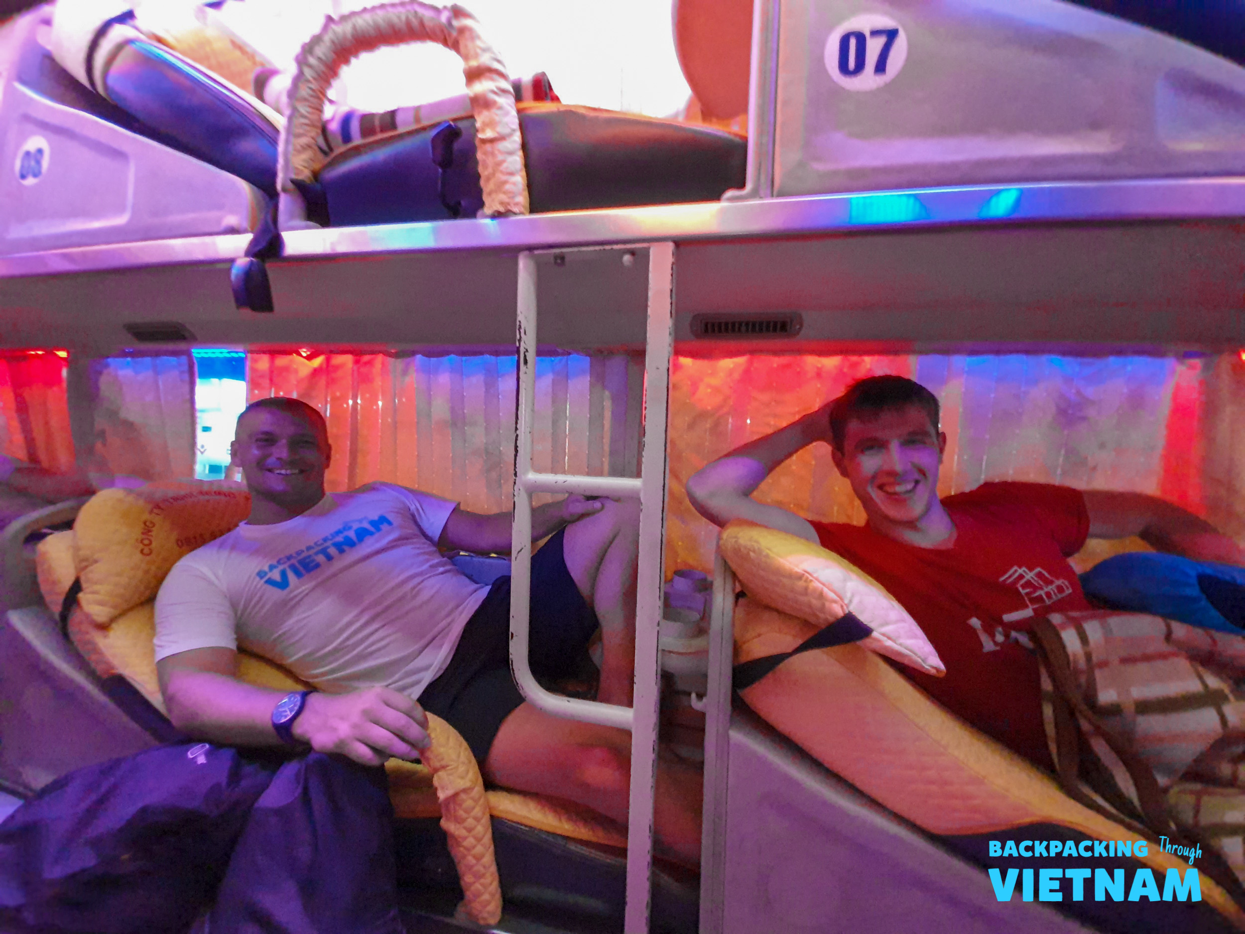 Two happy backpackers relax in their colorful sleeper bus bunks in Vietnam.