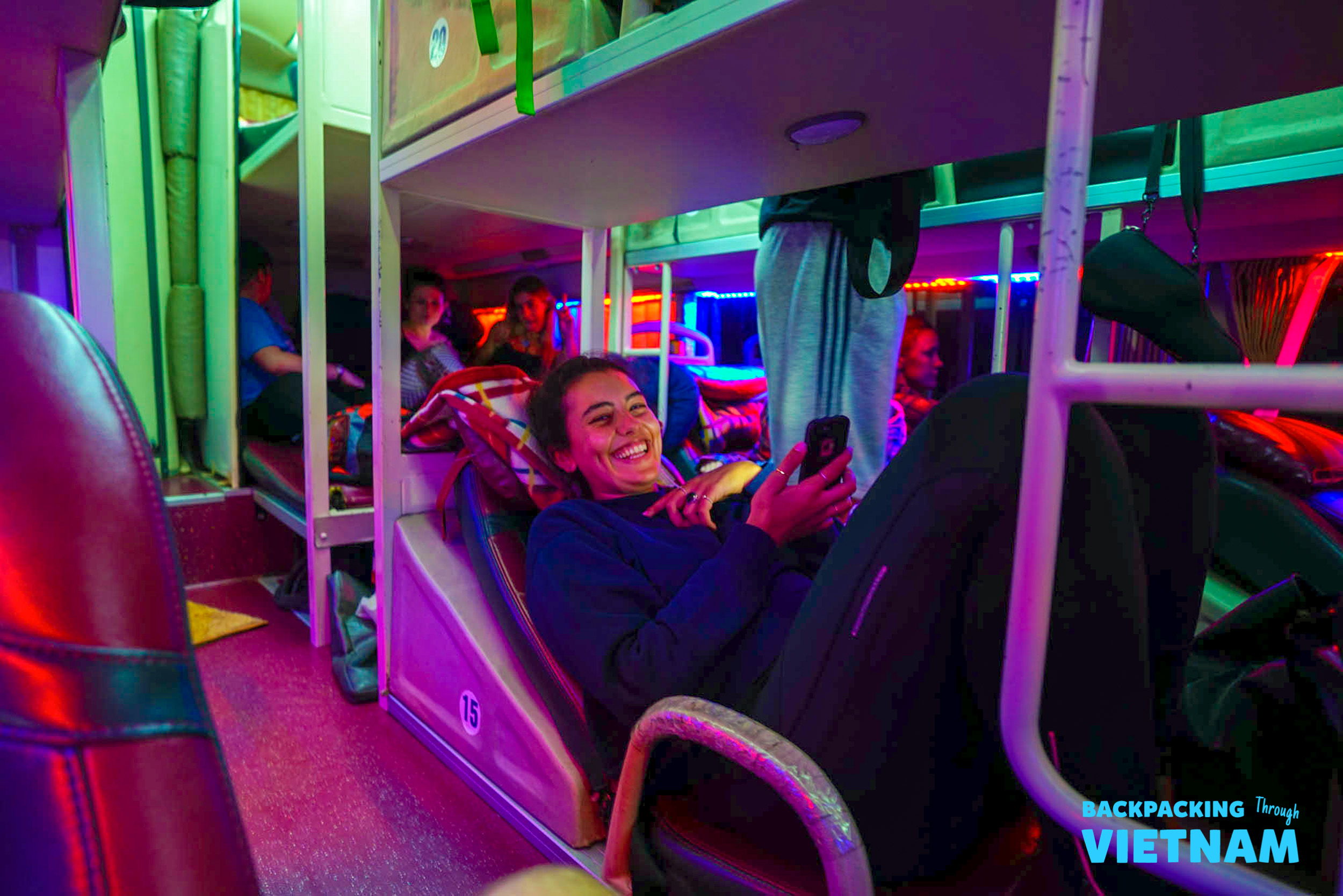 A smiling woman relaxes in a colorful bunk bed on a sleeper bus in Vietnam.
