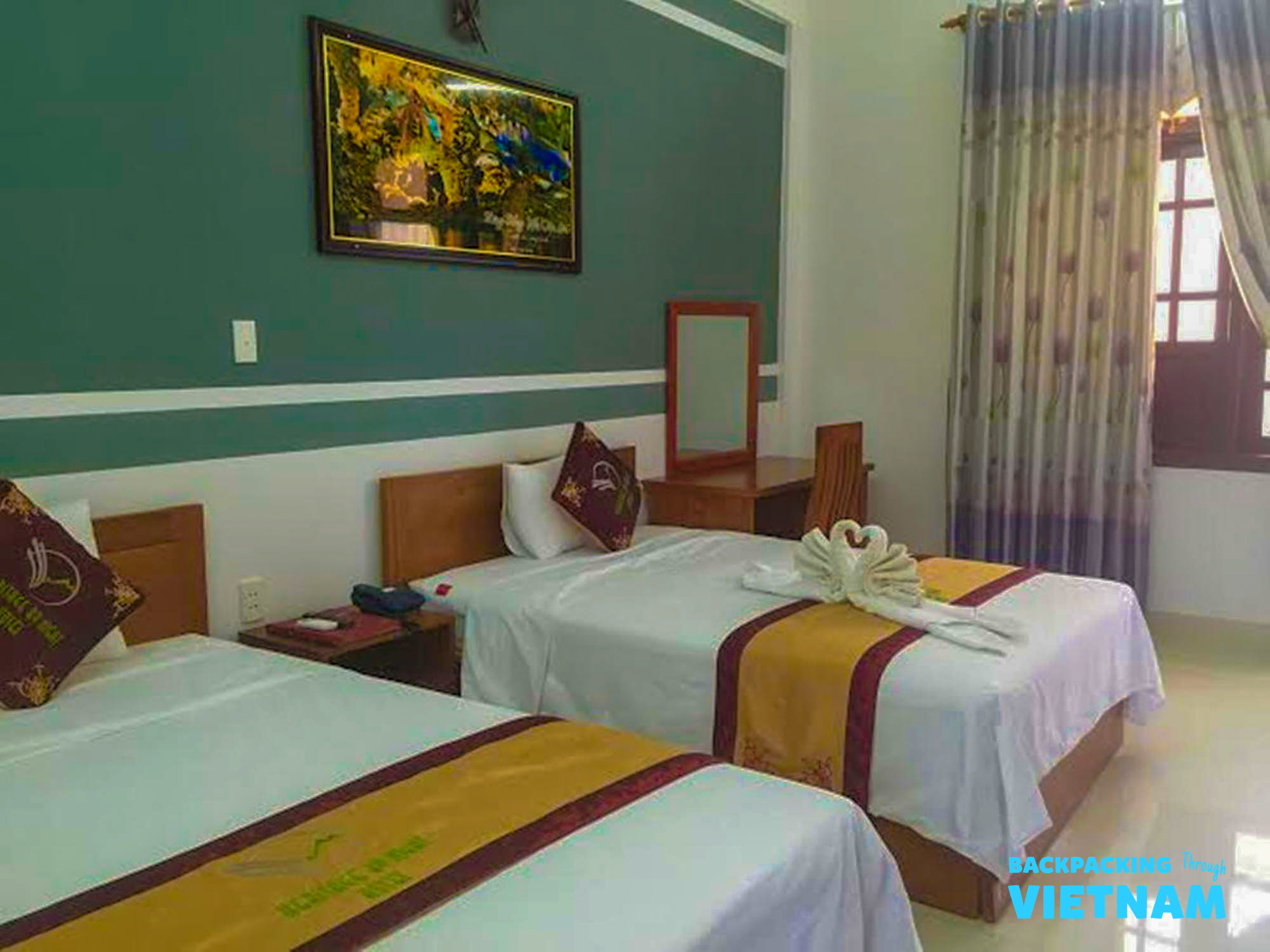 A welcoming hotel room in Phong Nha featuring two single beds with decorative runners and a window.