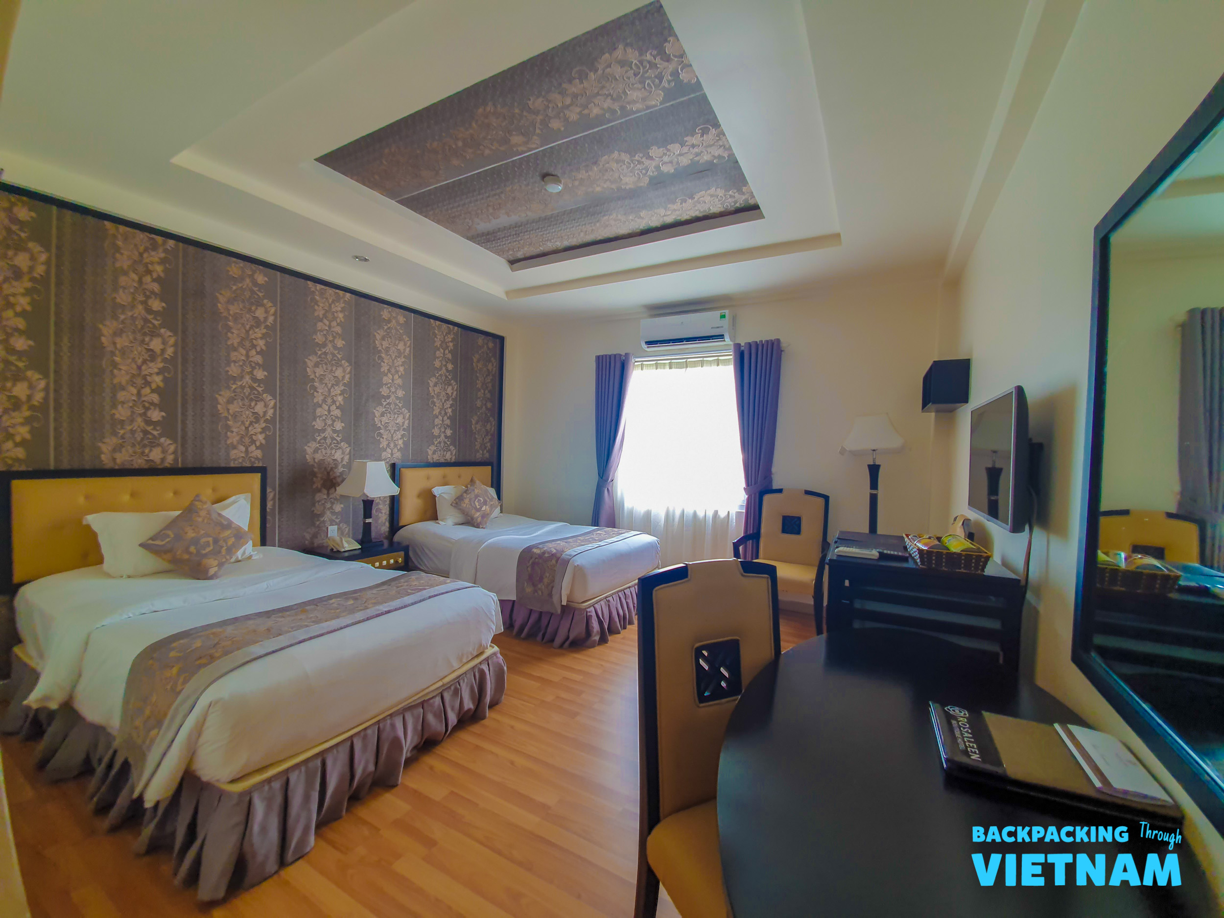 A comfortable hotel room in Hue with two single beds, a desk, and elegant patterned decor.