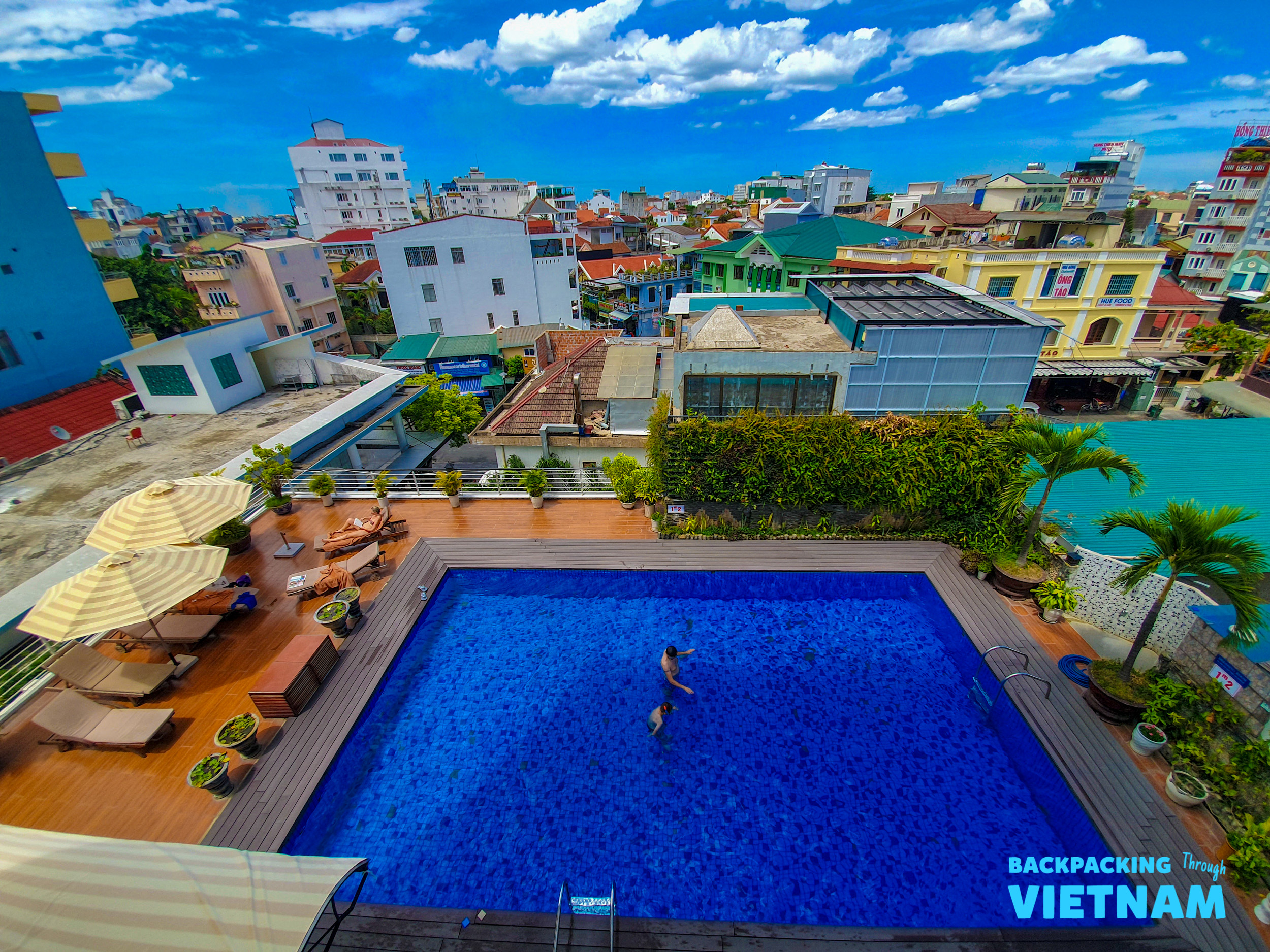 Two people enjoy a refreshing swim in a rooftop pool overlooking the city of Hue, Vietnam.