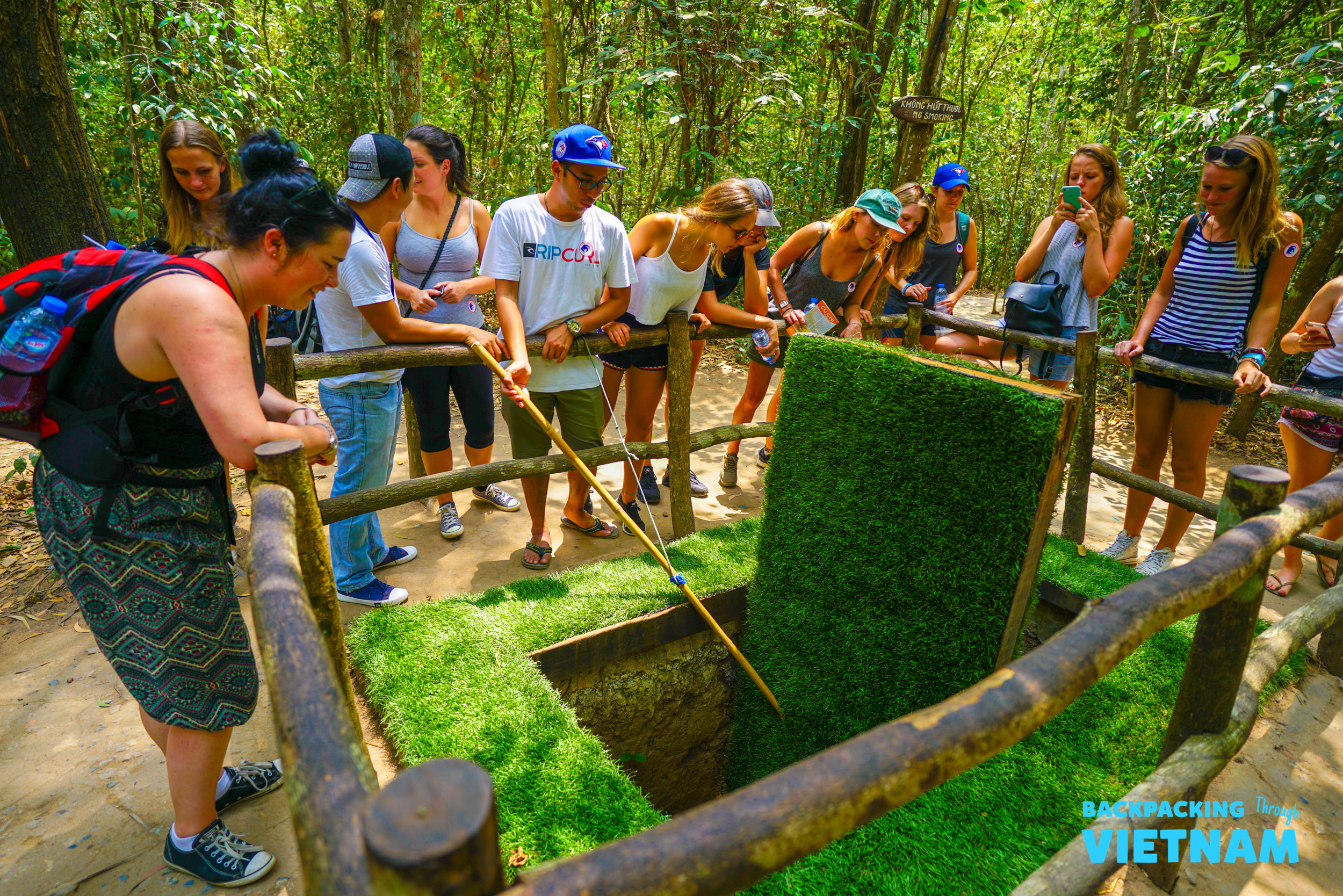 Curious travelers peer into a camouflaged tunnel entrance at the historic Cu Chi Tunnels near Ho Chi Minh.