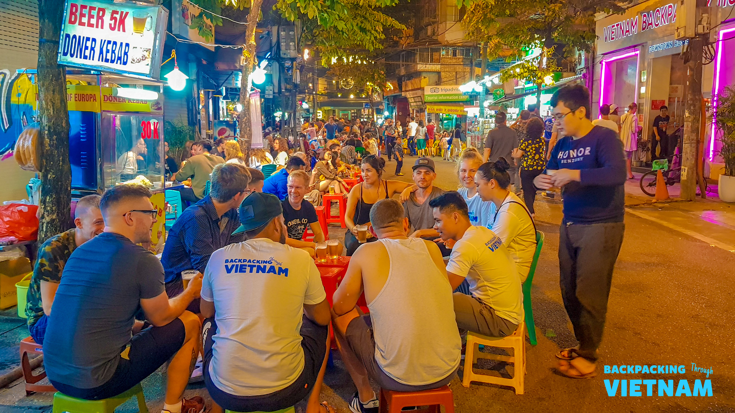 Backpackers enjoy a lively night out, sharing drinks and conversation on a bustling Hanoi street.