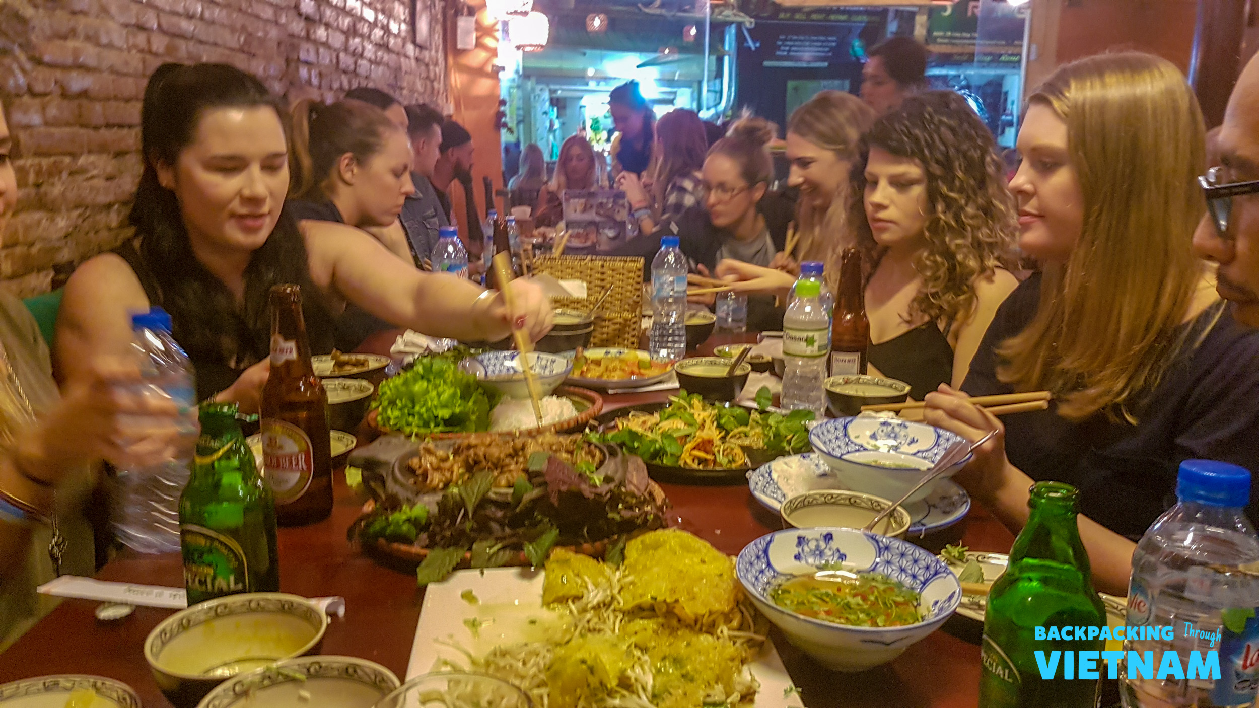 Backpackers enjoying a vibrant shared dinner with many local dishes in a lively Hanoi restaurant.