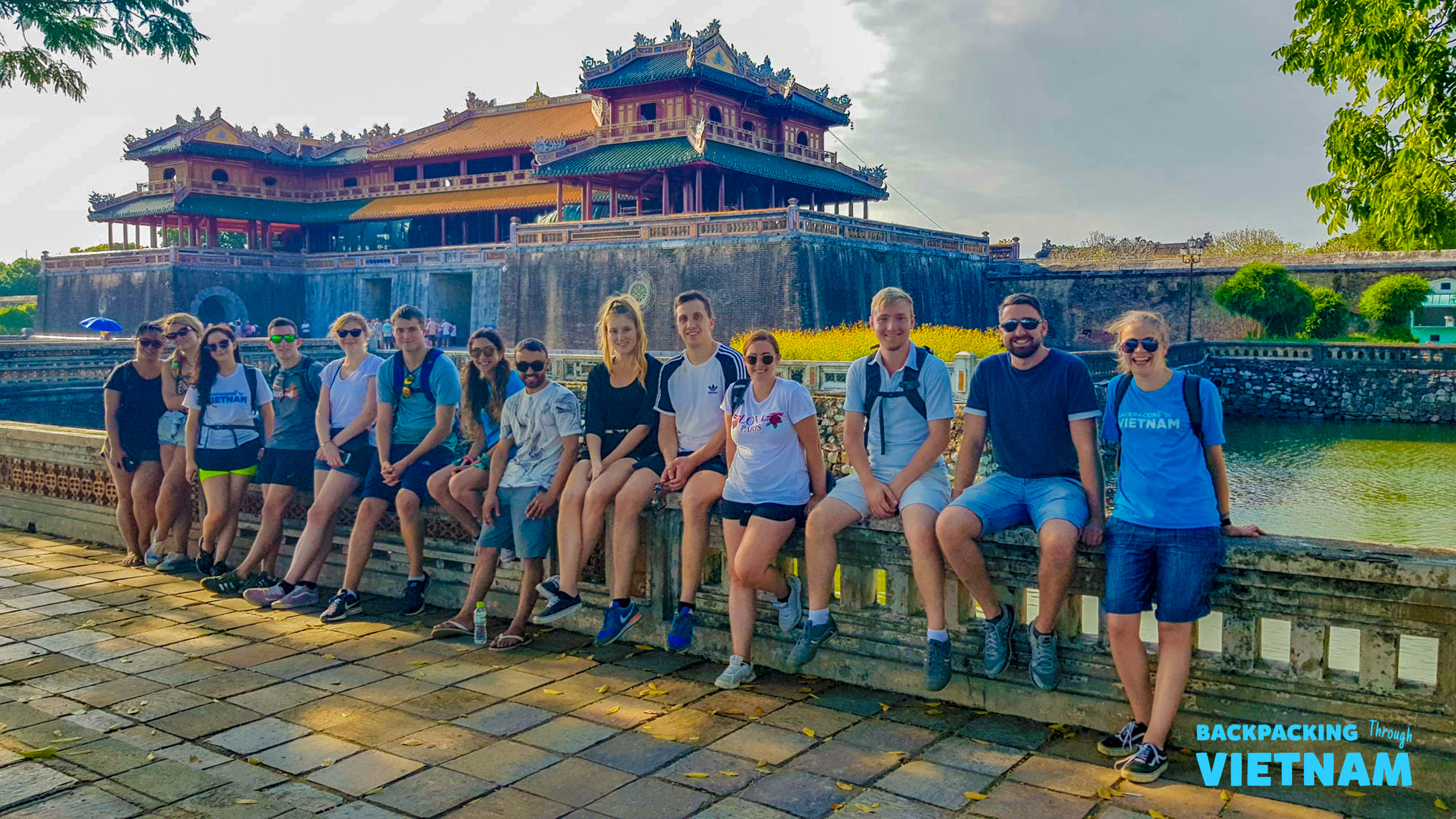 A group of happy backpackers sitting on a wall in front of the ancient Imperial City in Hue, Vietnam.