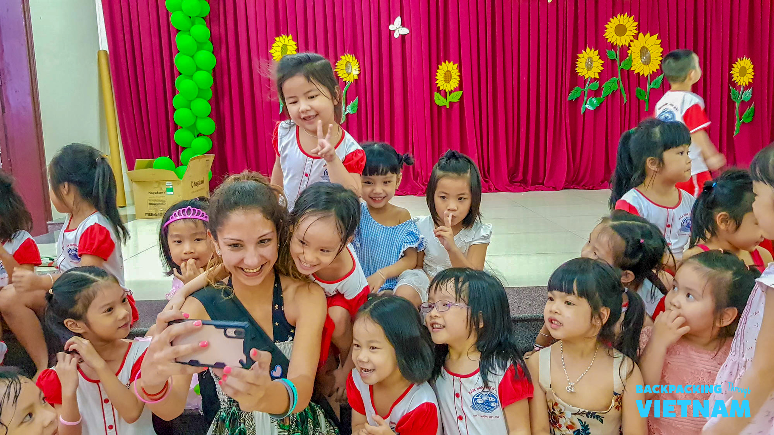 A backpacker takes a joyful selfie with a group of smiling Vietnamese children at a school in Hue.